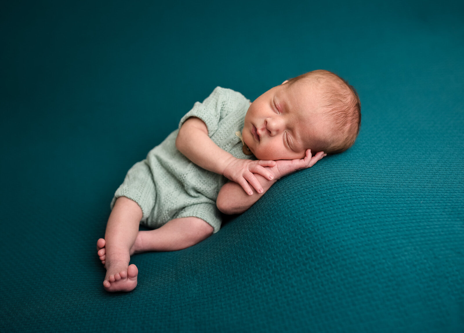 baby lying on teal blue blanket with green onesie