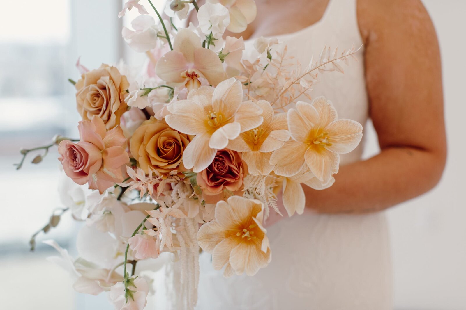 A peach, yellow, and pink bridal bouquet, up close and held by a bride on her wedding day.