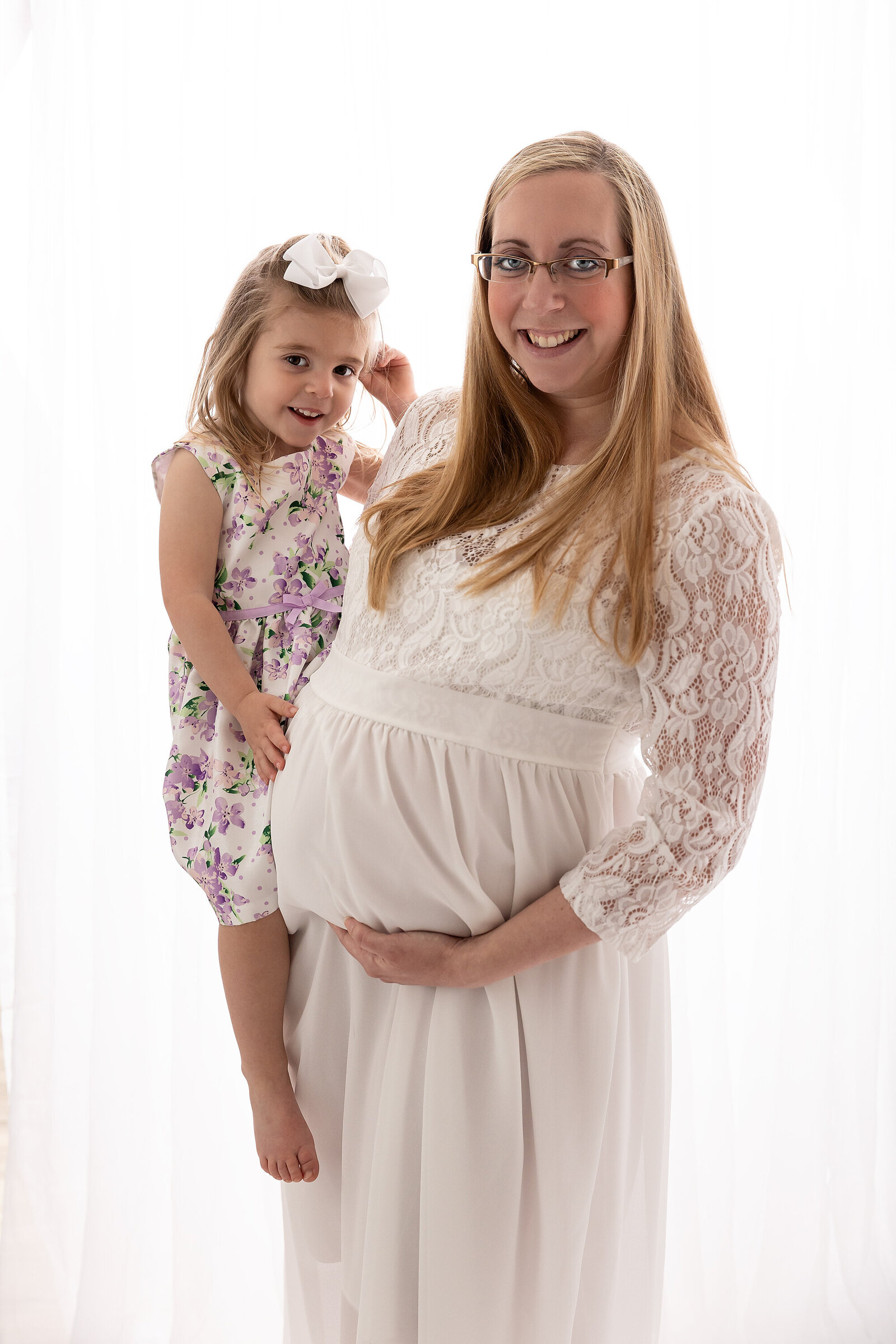 pregnant woman in white lace dress holding baby belly and toddler