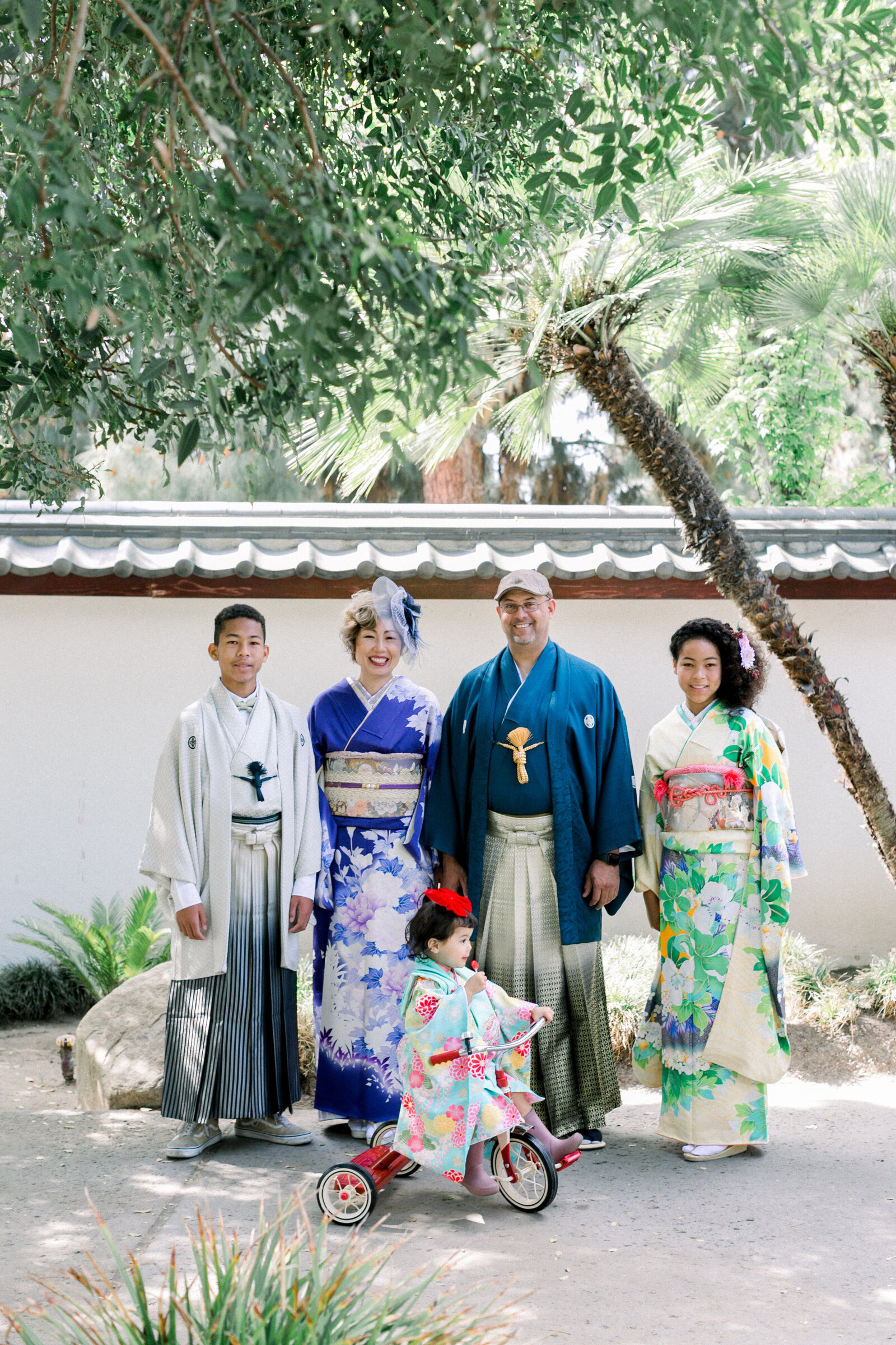 Elegant family portrait at Brand Park’s Shoseian Whispering Pine Japanese Tea House for a Seijinshiki (coming-of-age) celebration—mother in purple kimono, daughter in green-and-yellow furisode, son in white hakama, and little girl in pastel kimono, kimono rental in Los Angeles | ロサンゼルス・ブランドパーク松聲閣での成人式家族写真。紫の着物の母、緑と黄色の振袖の娘、白袴の息子、淡い色の着物の幼児、着物レンタル
