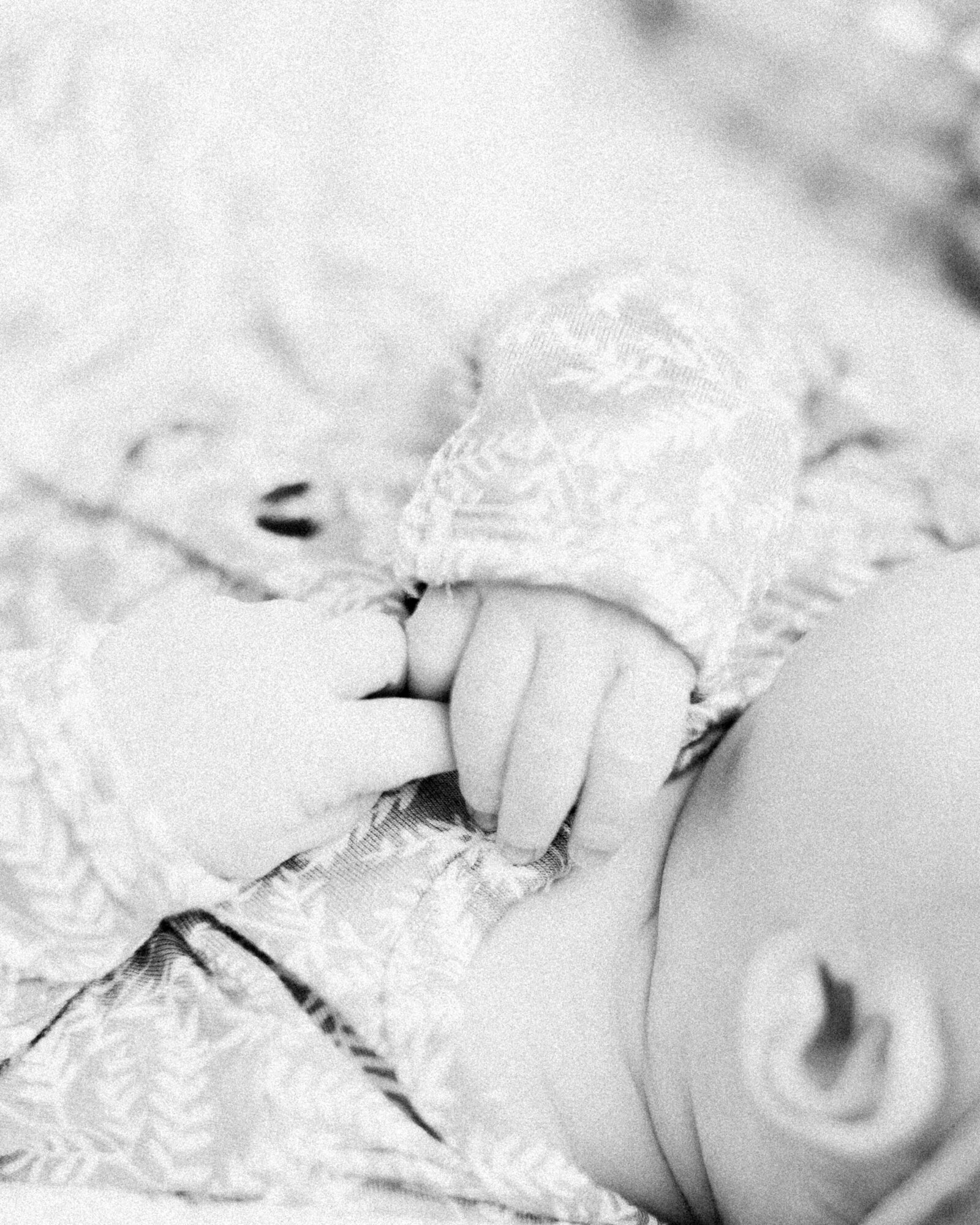 Closeup detail in black and white with film grain of baby grasping her hands by NH newborn photographer Fieldstone Studio.