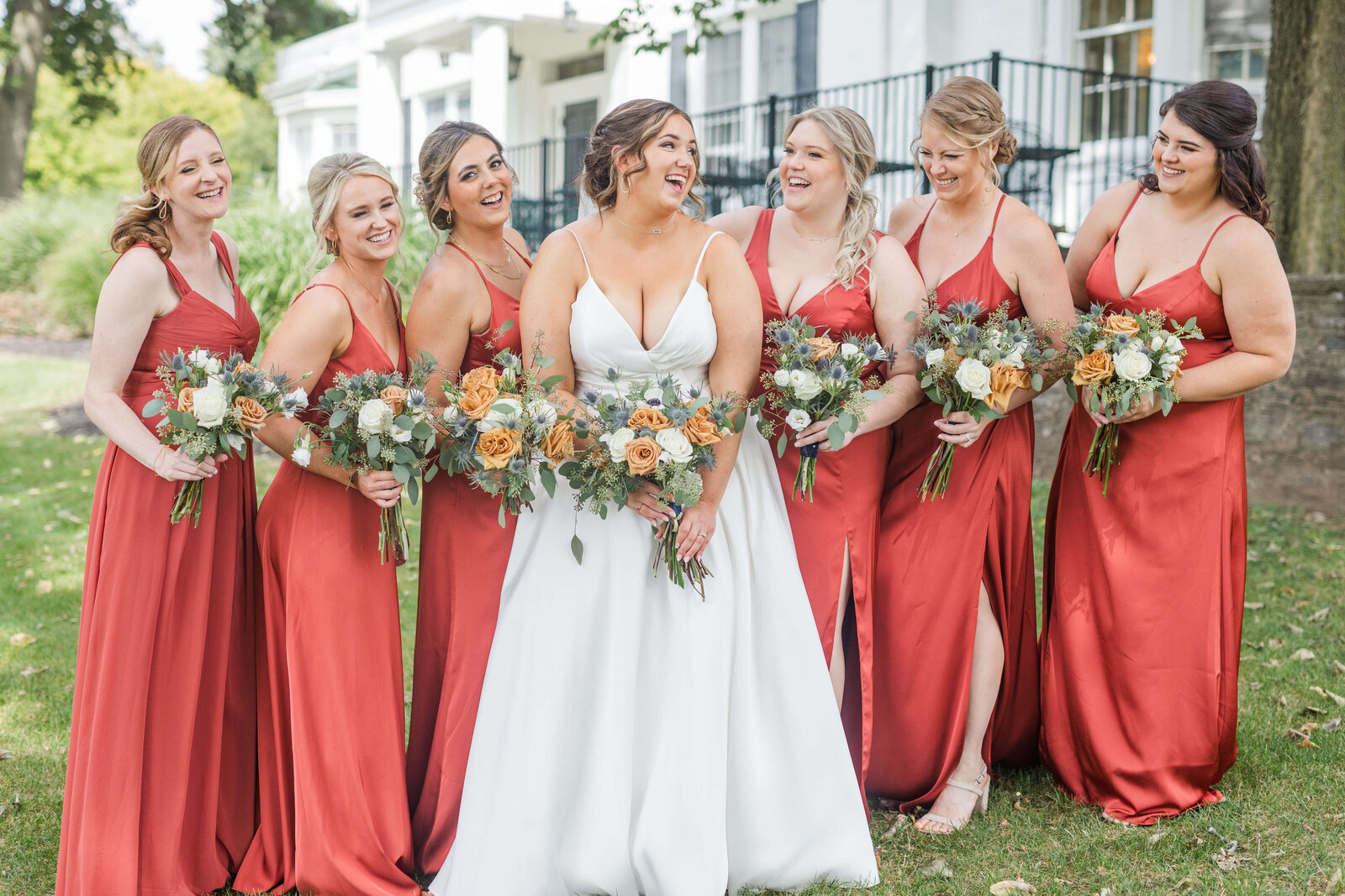 Bride and bridesmaids in orange dresses holding bouquets and laughing. At venue Walden Ponds.