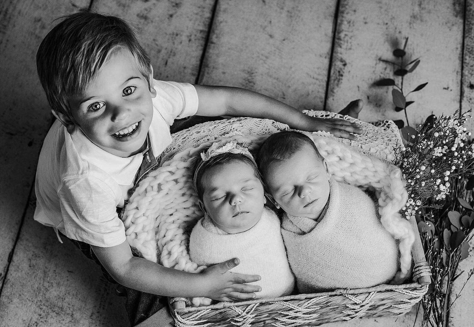 In a cozy home setting, a little boys snuggle his newborn twin siblings in a basket, captured by Bia Schaefer Photography, Orlando’s best newborn photographer.