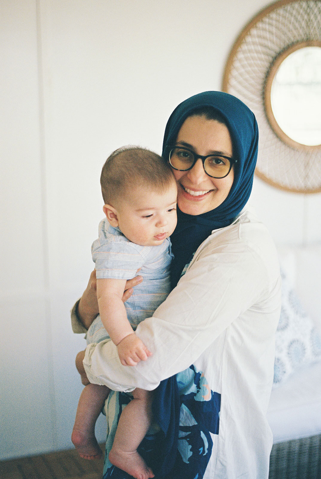 Mother holding her baby in a soft embrace, wearing a vibrant blue hijab with a natural background.