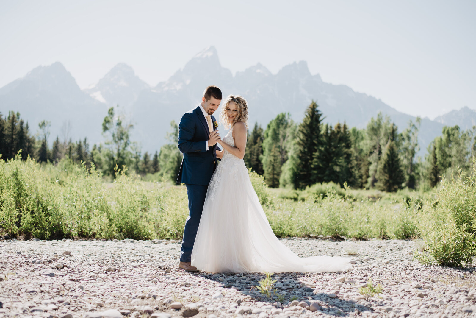first dance as husband and wife at grand teton wedding with bride and groom together holding hands and talking as they dance in a green field in front of the Tetons