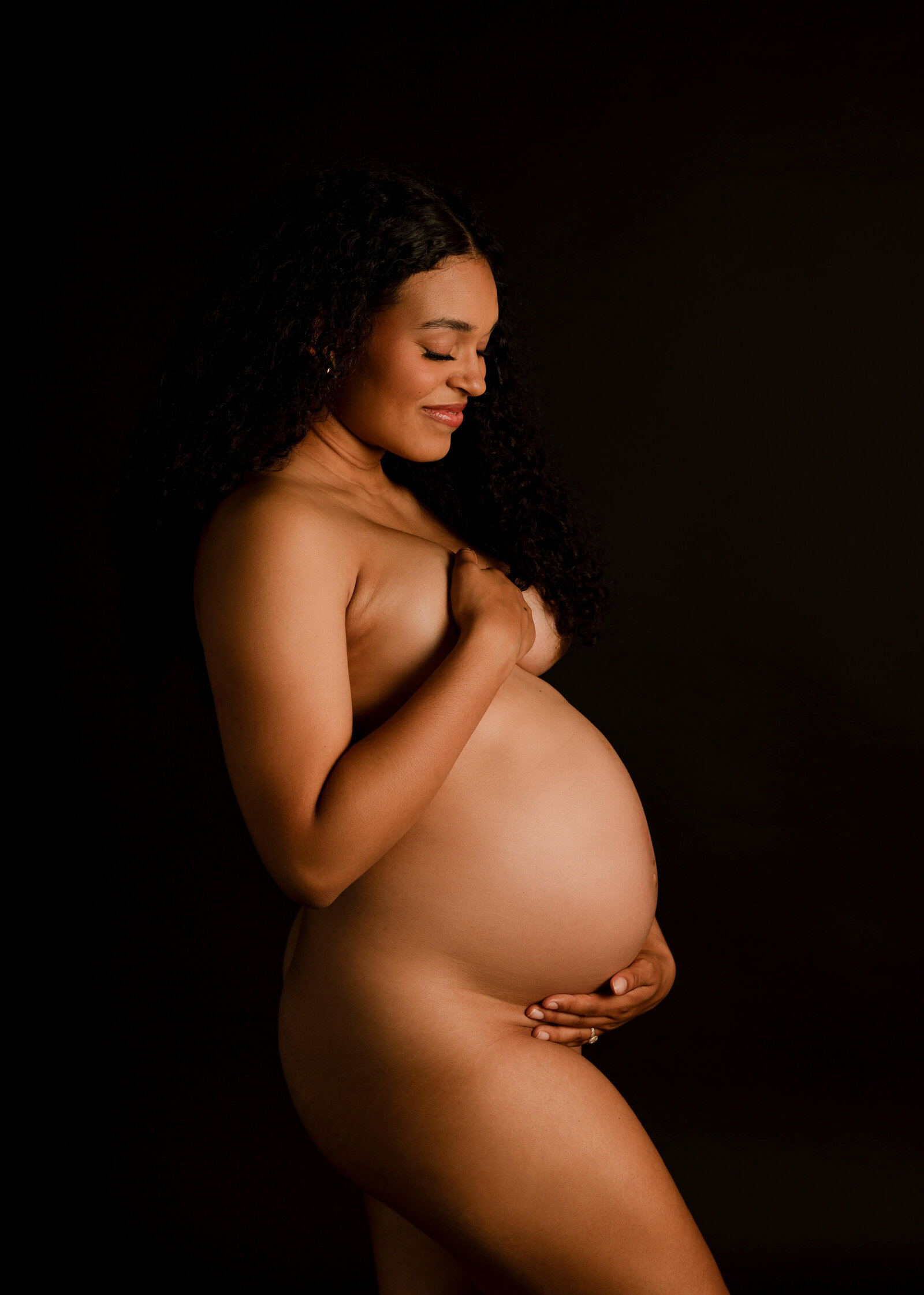 Momma standing nude in studio looking down at belly smiling by Ashley Nicole Photography