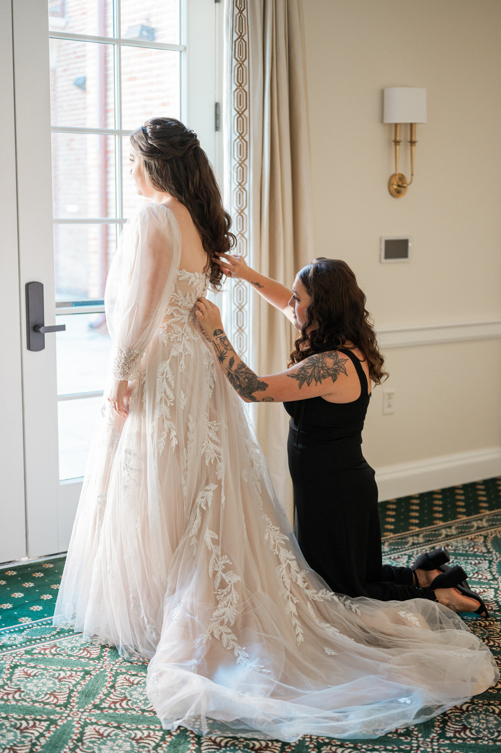 A person on their knees helping a bride zip her wedding dress