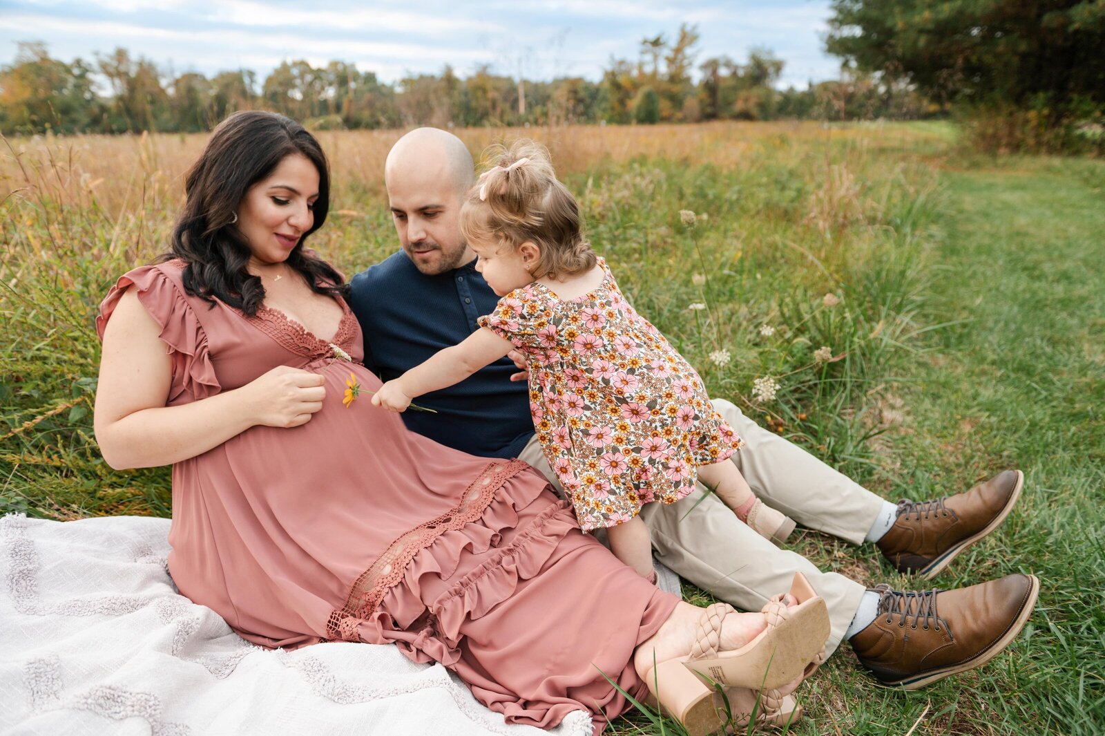 3 year old girl pointing to her moms belly during maternity session in field