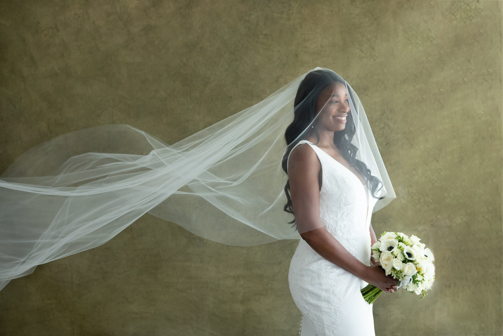 bride wearing a veil that is blowing in the breeze and holding a bouquet