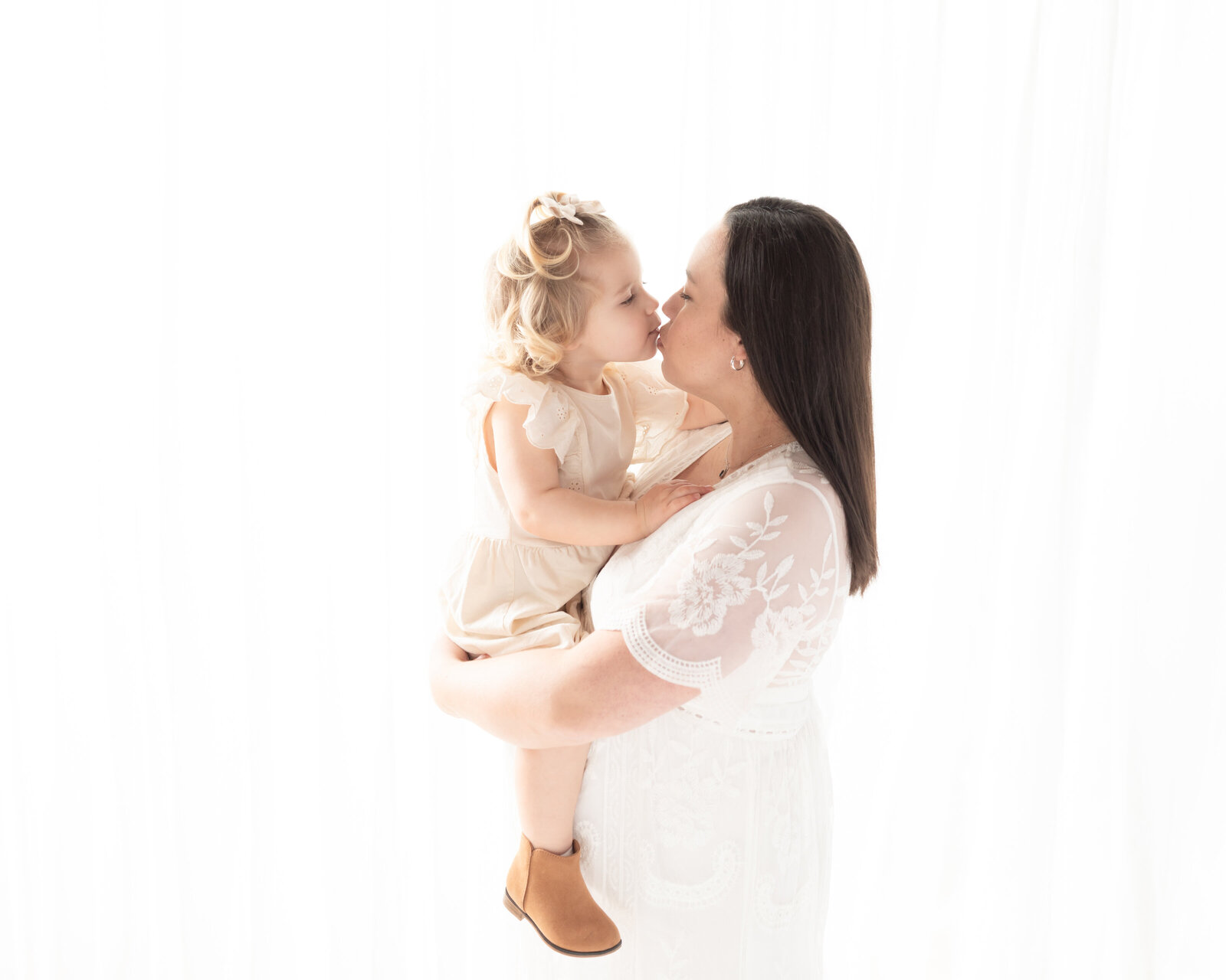 pregnant mother in white lace dress holding daughter for maternity portraits