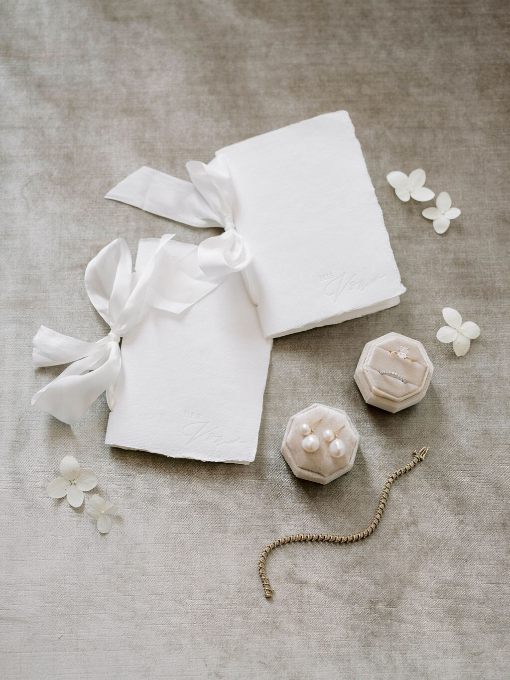 Flat lay of vows, jewelry, and small white petals.