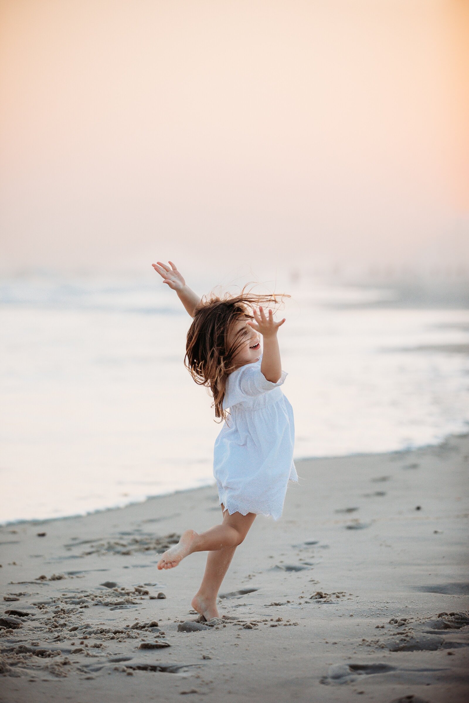 Pensacola Beach Family Photography session with little girl dancing in the sand at sunset.