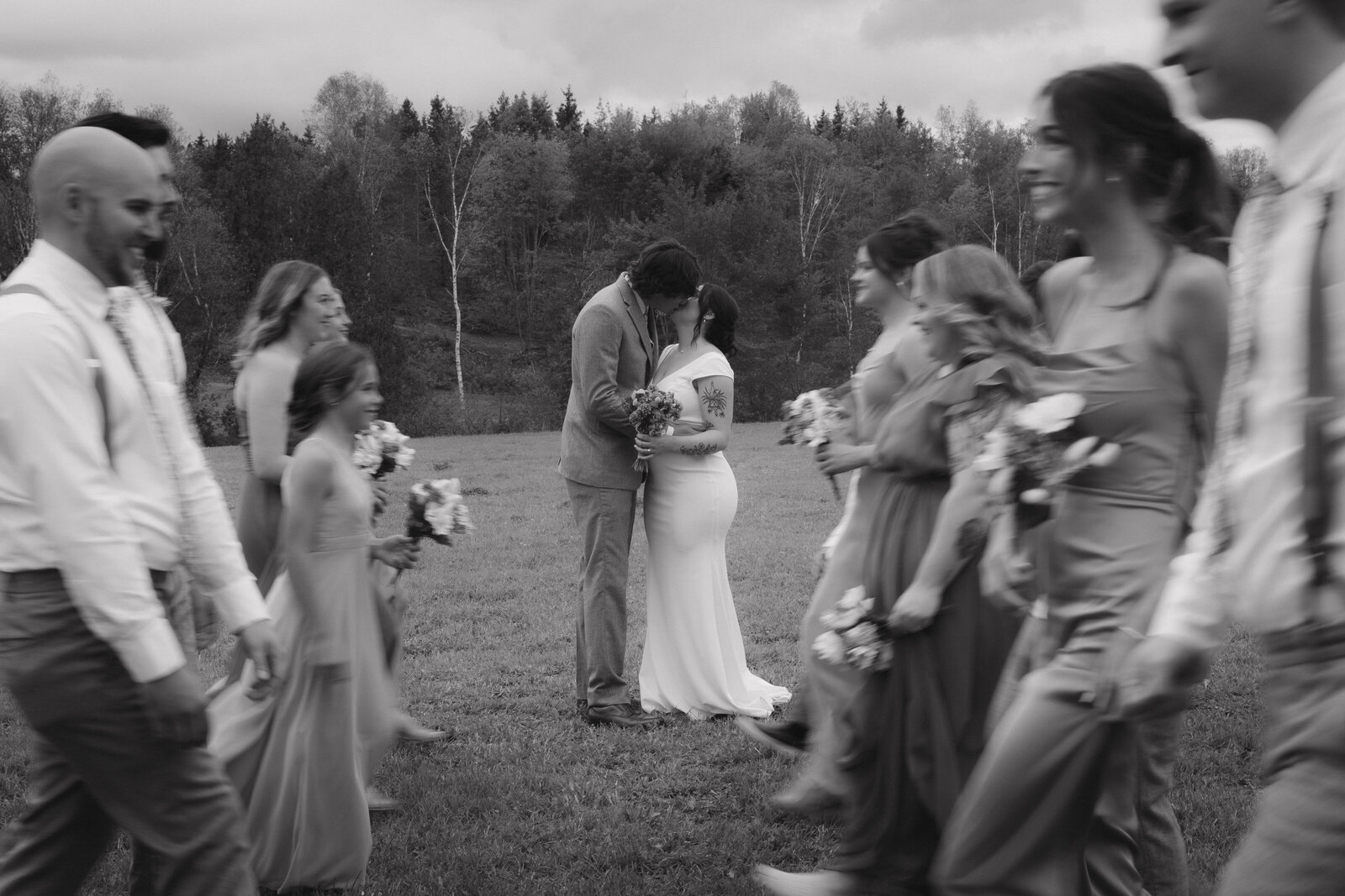 bride and groom kissing while their bridal party walks around them at their wedding in maine