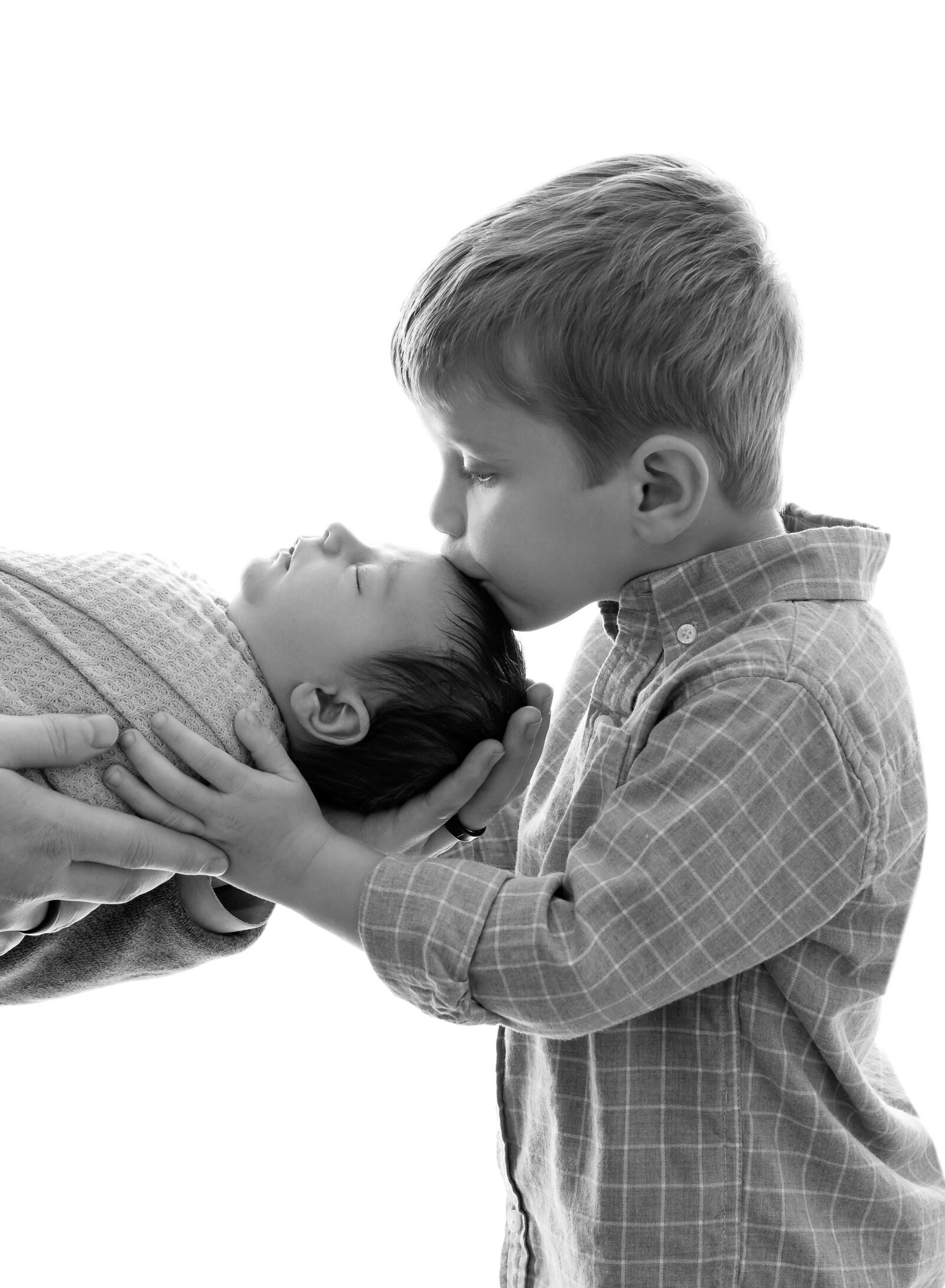 Dad holding newborn baby with brother kissing baby's head. Photographed at Atlanta Baby studio.
