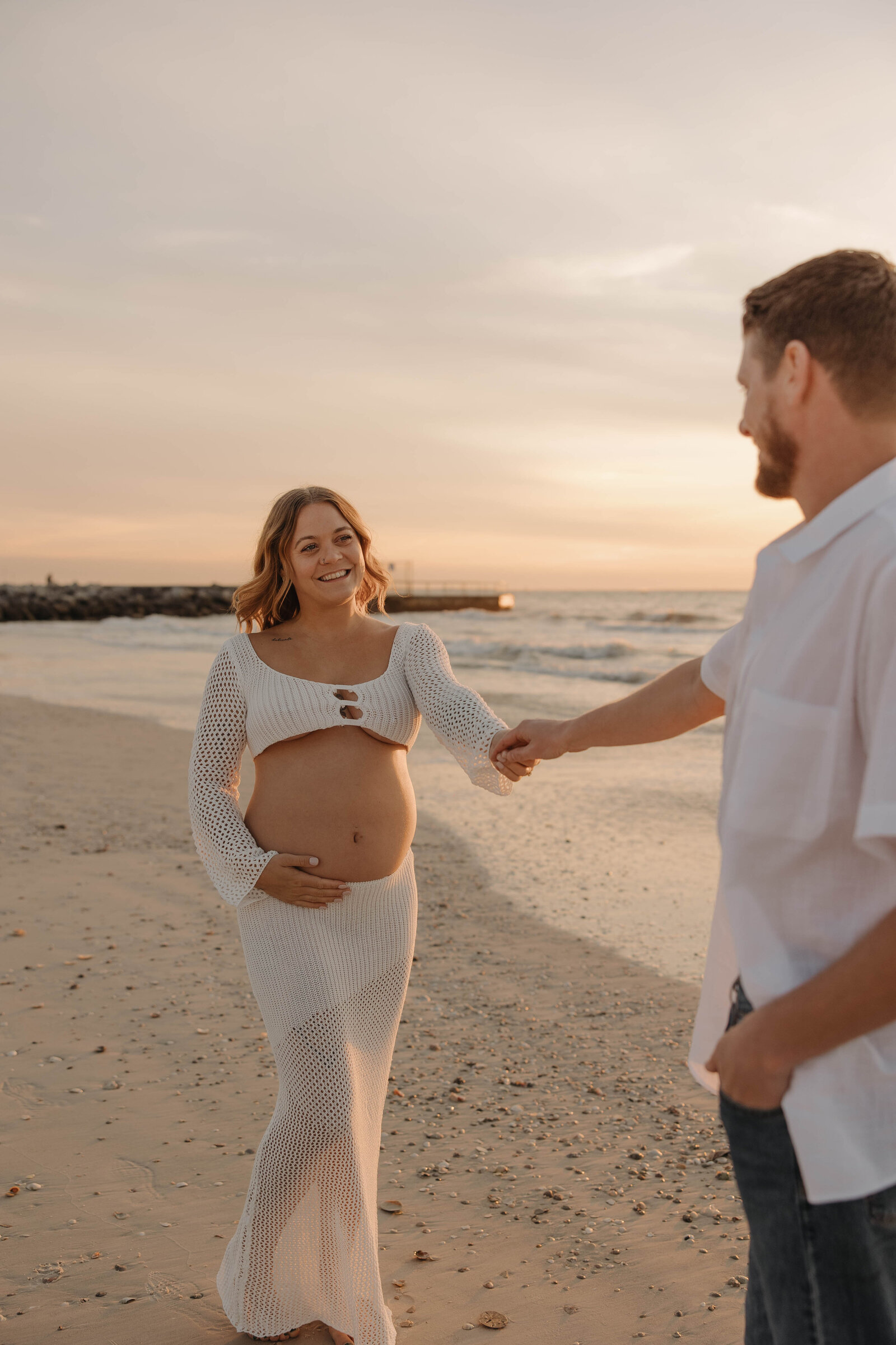 A couple during a maternity photography shoot at sunset on the beach.