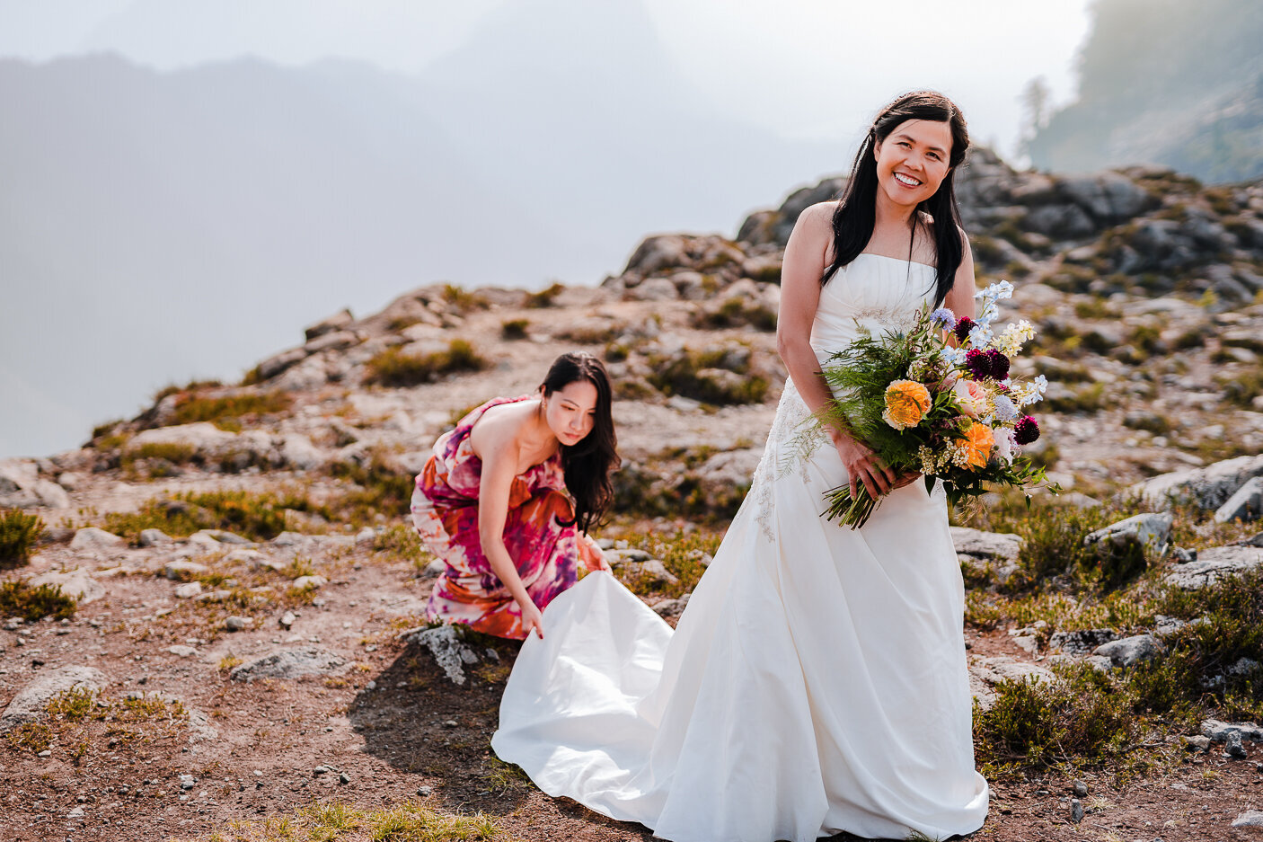 Bridesmaid fixing bride's dress during an elopement photoshoot in Baker WA.