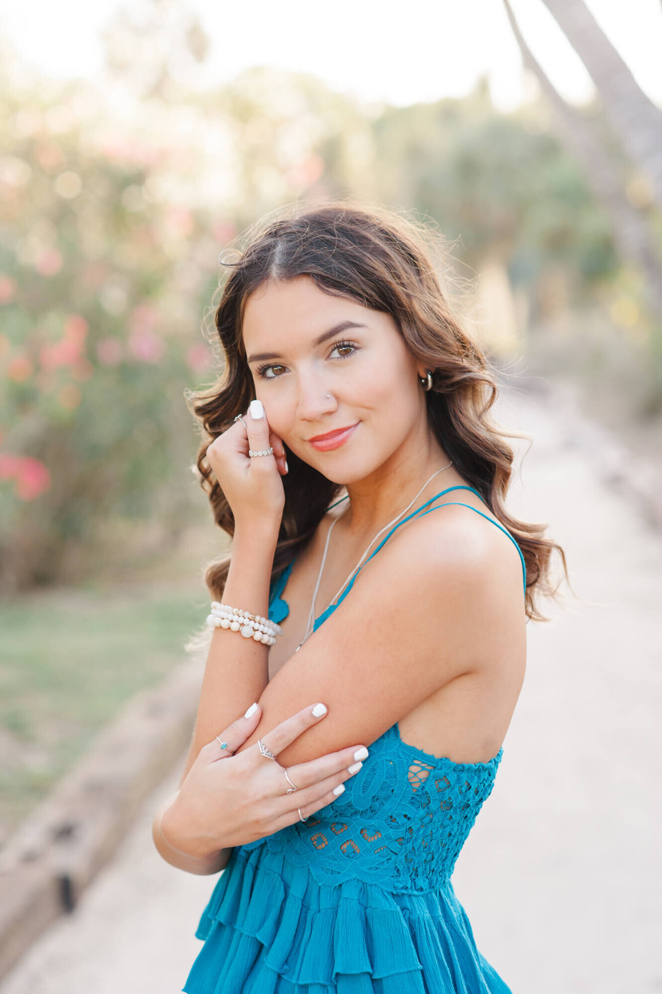 Senior girl stands posing for a portrait with her hand on her cheek on beach path