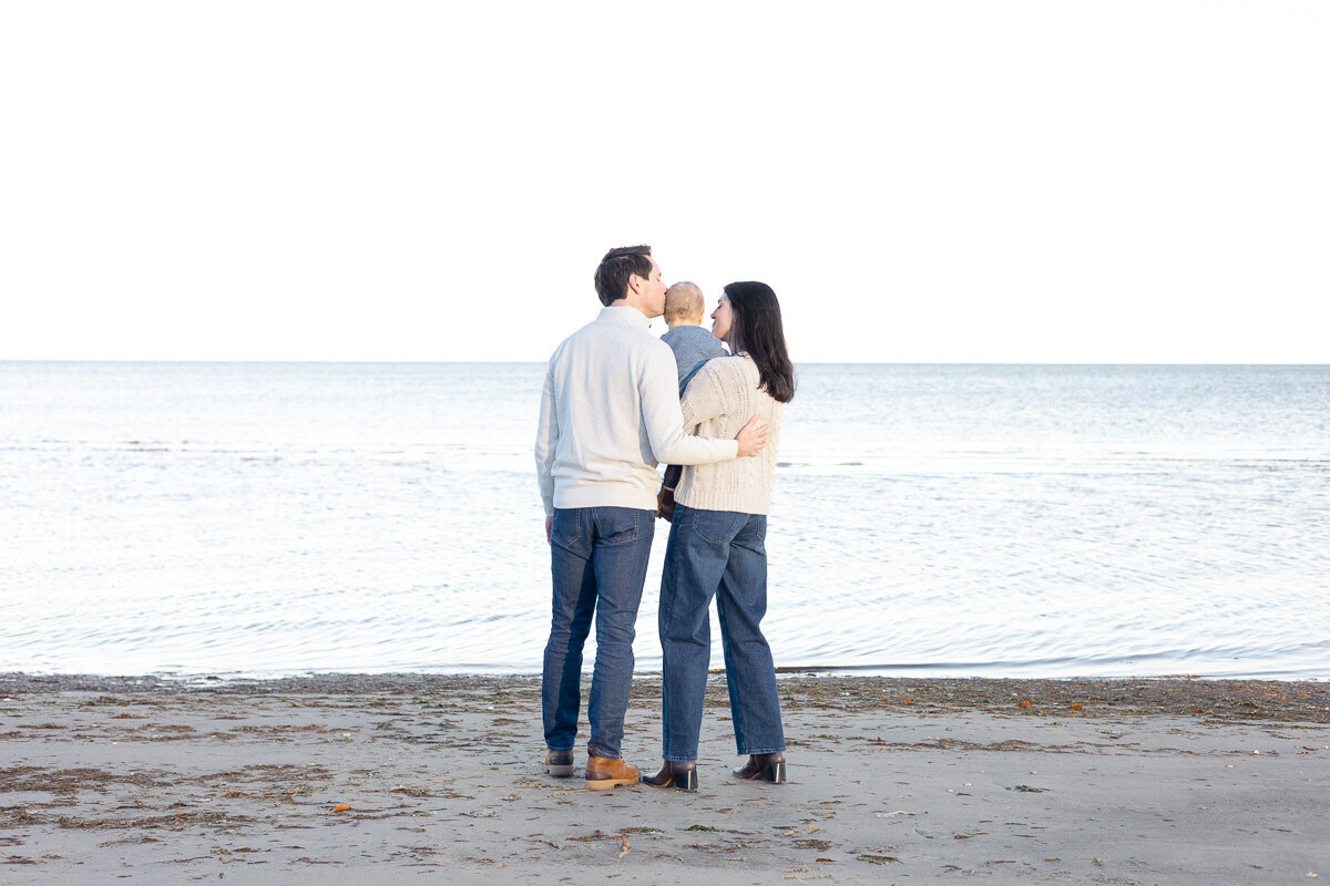 Family standing together at the water’s edge during a beach family photo session in Fairfield County, CT. Captured by Nicole, a lifestyle family photographer for parents who want heartfelt, natural moments frozen in time.