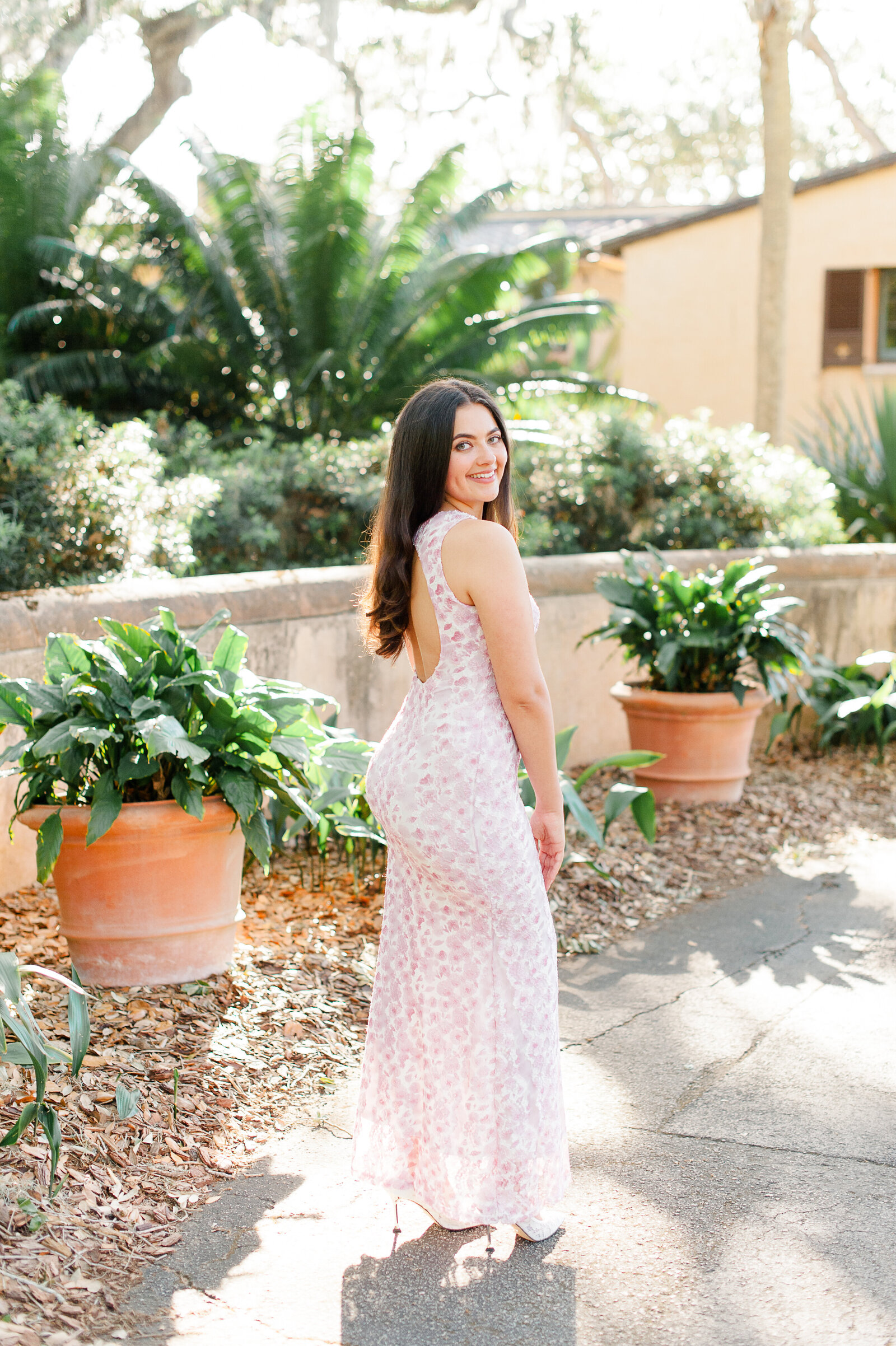 Senior girl standing in front of beautiful gardens smiling at the camera