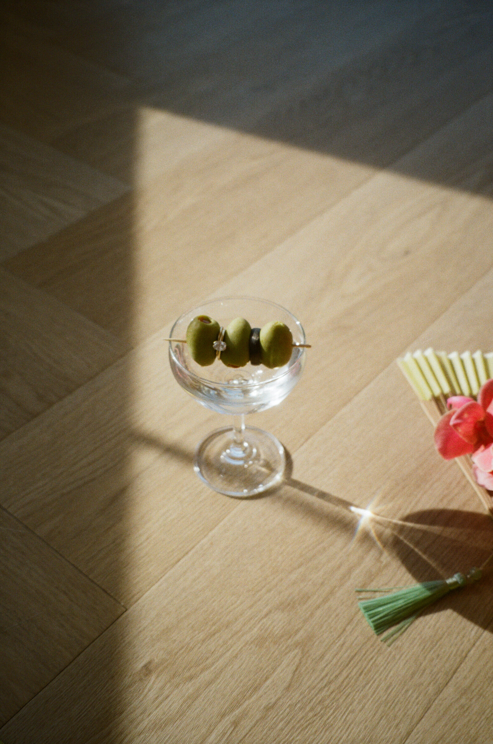 A film photo of a coup with a stem full of olives which is holding a beautiful engagement ring at Cidery 51.