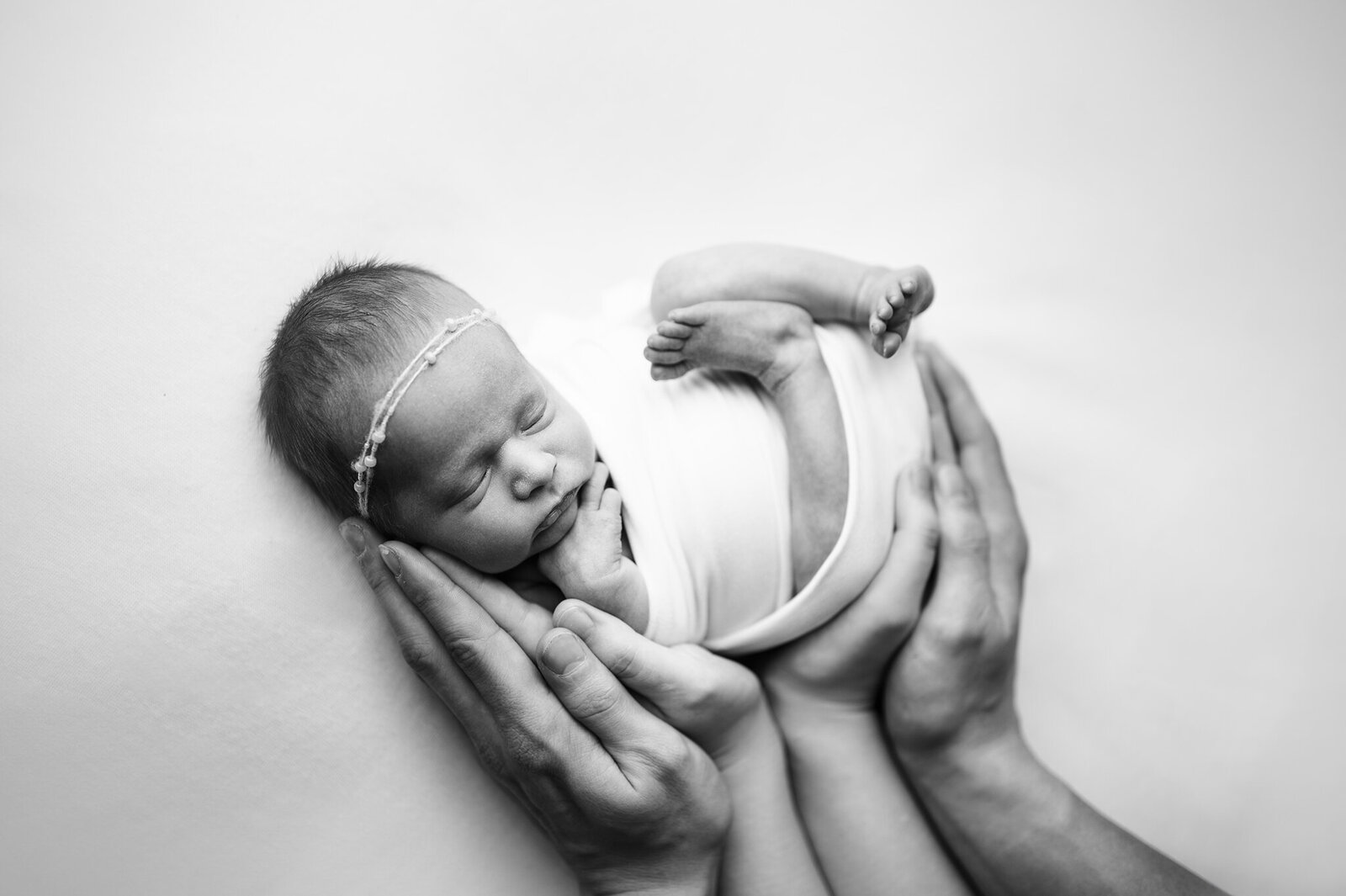 Explore our exquisite newborn photography services in Grand Rapids. This serene black-and-white image captures the tender moments of a newborn cradled in loving hands, showcasing the delicate beauty and peacefulness of early life. Book your session today to preserve these precious memories with professional, patient, and dedicated photography