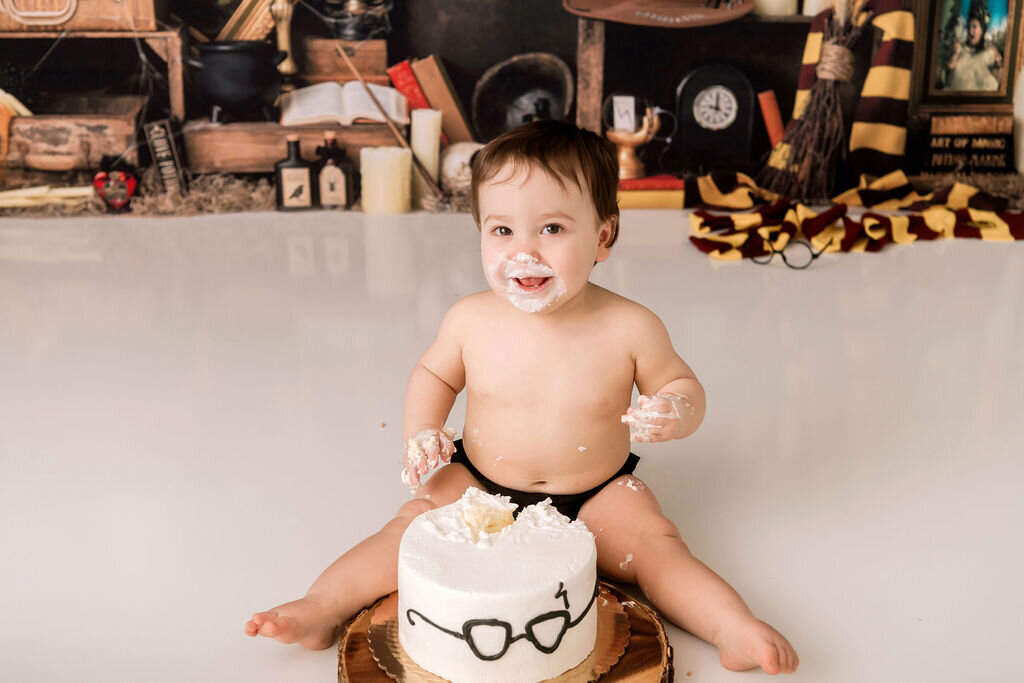 Baby boy enjoying cake smash session with glasses-themed cake during first birthday portrait session
