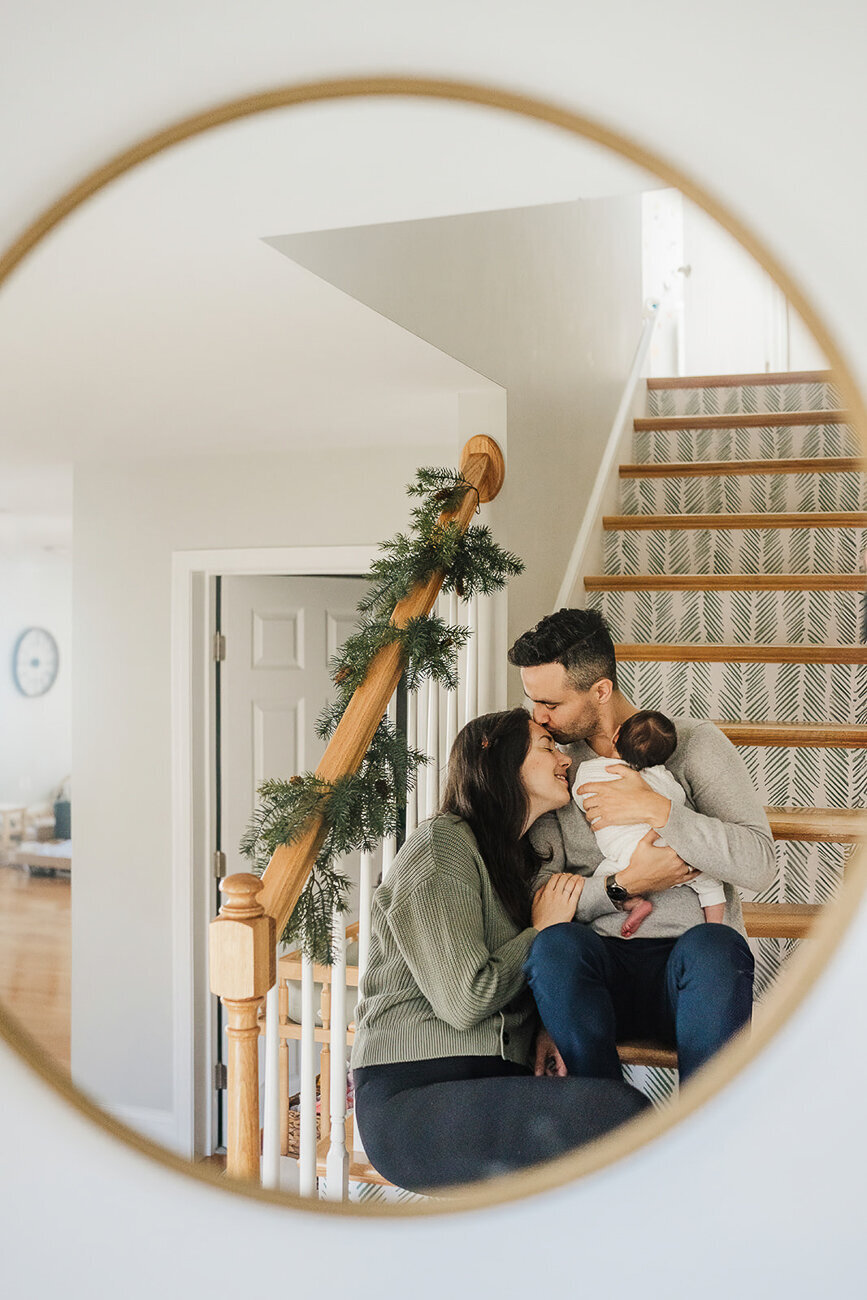 image through mirror of parents snuggle on stairs with new baby