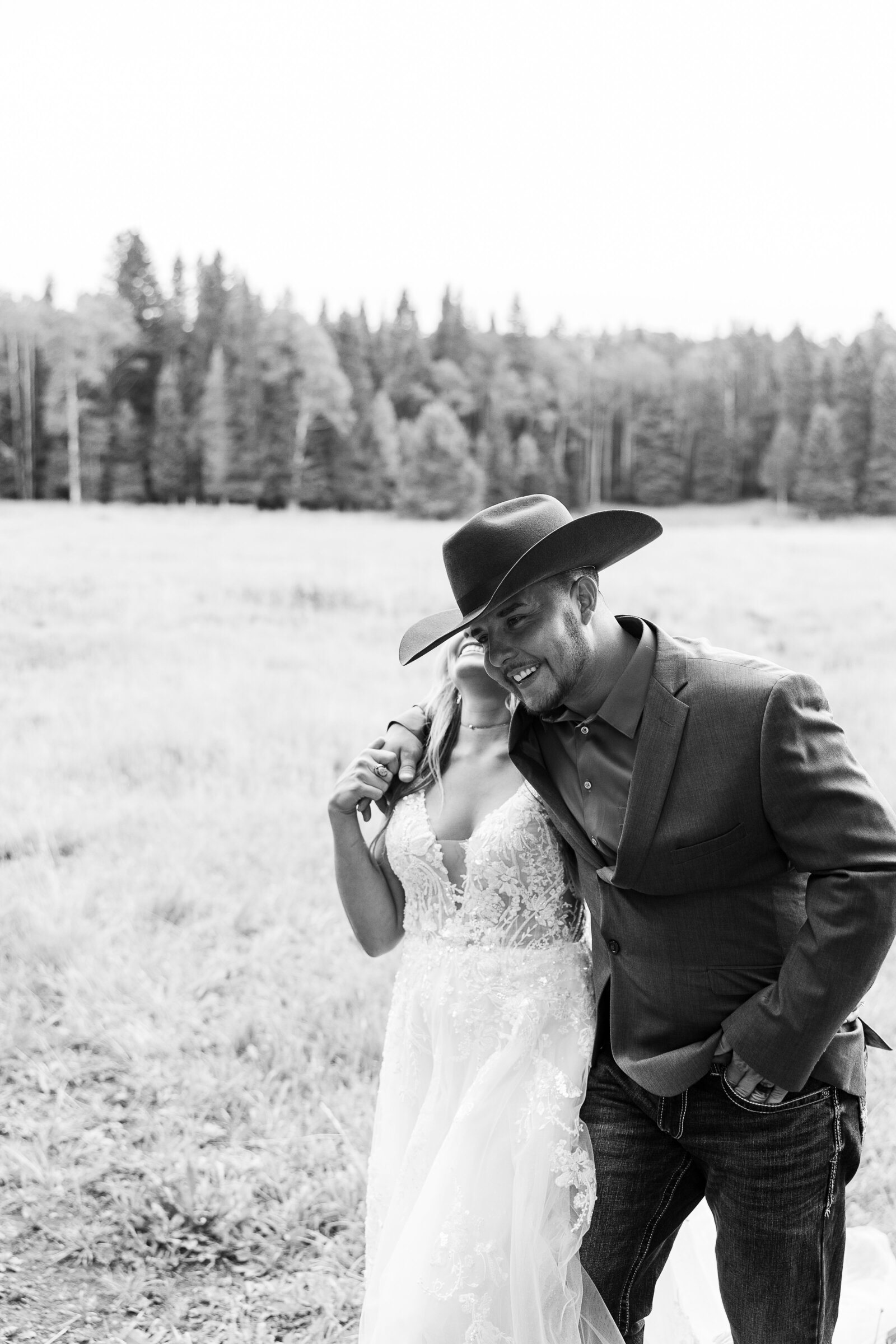 Black and white image of grooms hand over bride walking and laughing in field