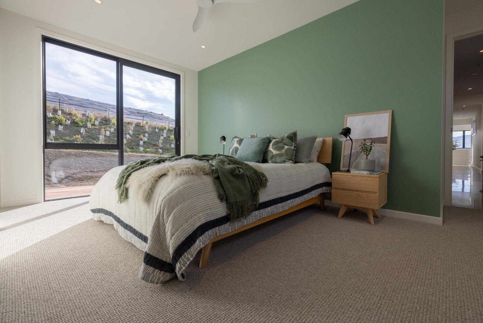The master bedroom featuring light carpet and a green feature wall in a home built by Twin Peaks Construction Queentown.