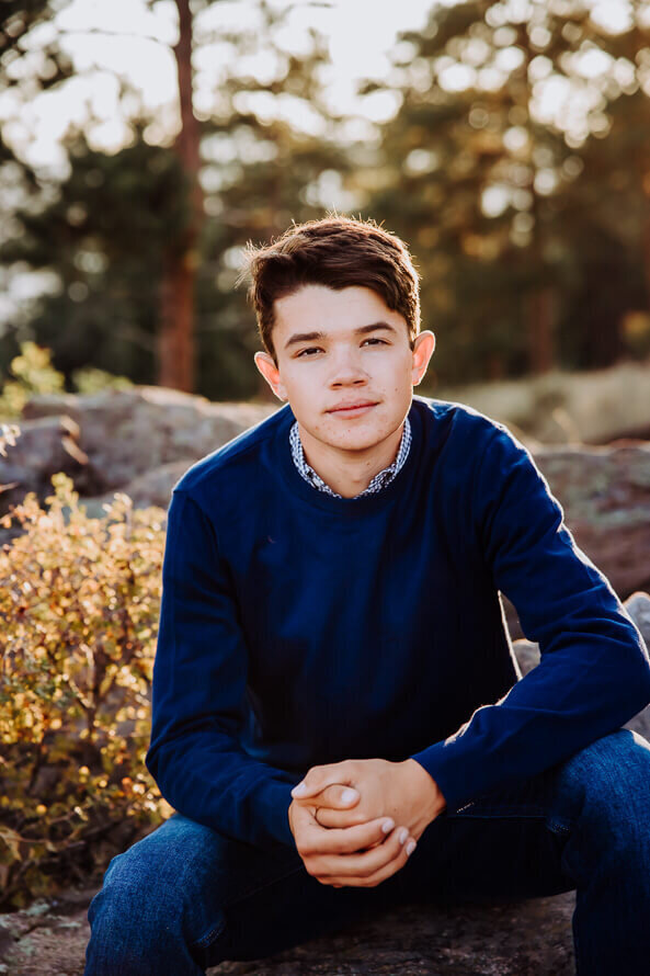 Boy in blue sweater folds hands and looks at camera at Mt. Falcon Park.