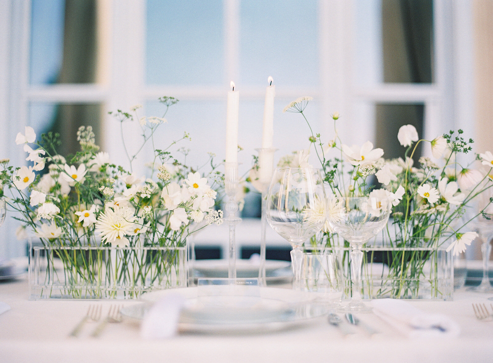 All white and green center pieces of reception table. Clear vases with individual floral stems through each opening in vase. Photographed by Amy Mulder Photography