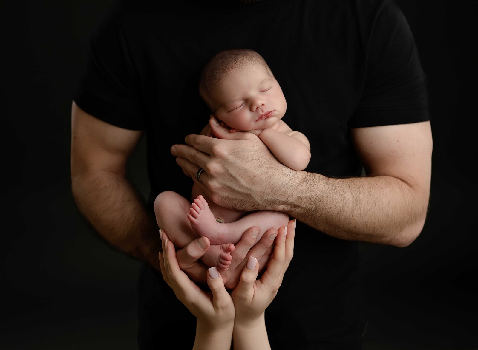 Naked baby girl being held in dad's arms with Mom's hands cradling her. Photo taken at Newborn Photography studio in Atlanta, GA.