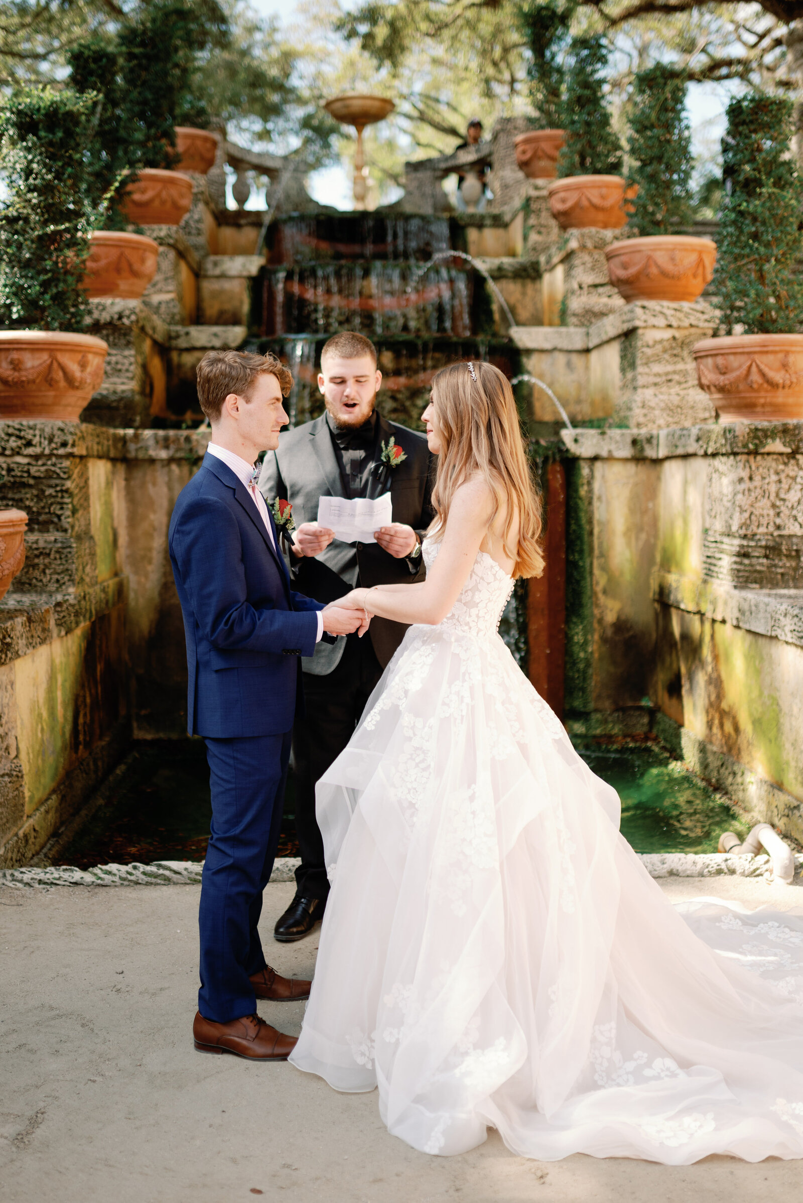 Bride and groom standing at their altar, in front of a fountain in the garden at Vizcaya