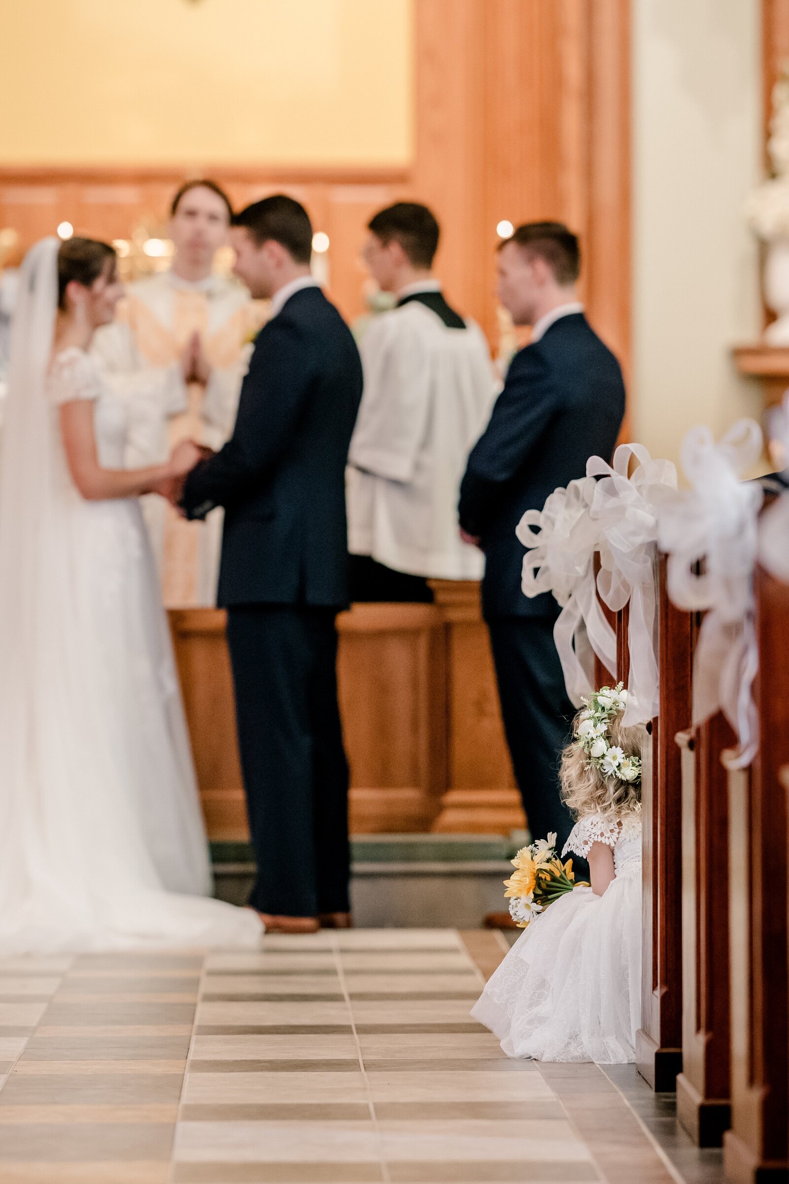 A flower girl peeking out into the aisle during a Catholic wedding in Northern Virginia