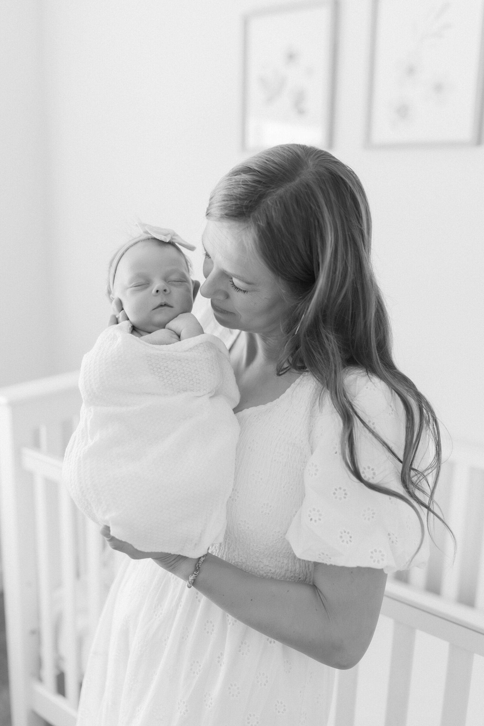 Mother holding newborn baby in softly lit nursery, captured by a newborn photographer in Salt Lake City – tender moment with natural light and calming neutral tones