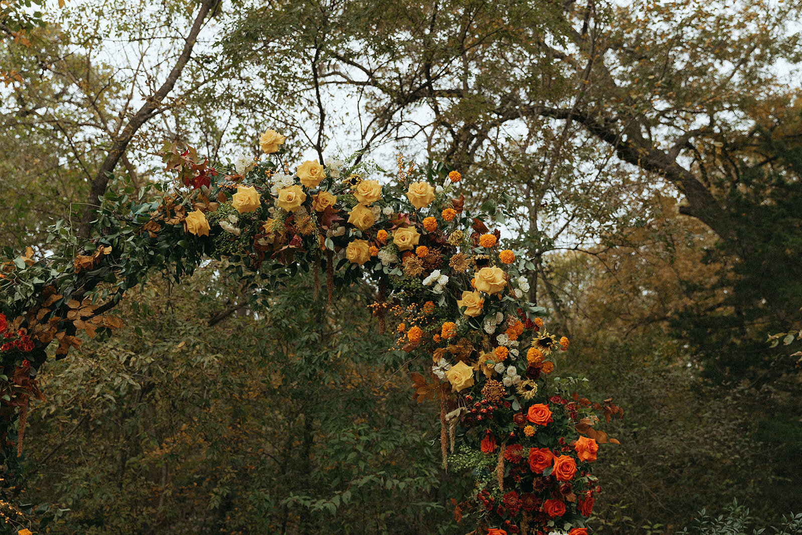 Fall wedding arch installation with vibrant seasonal flowers in rich autumn hues, designed by The Floral Eclectic at a Dallas outdoor venue