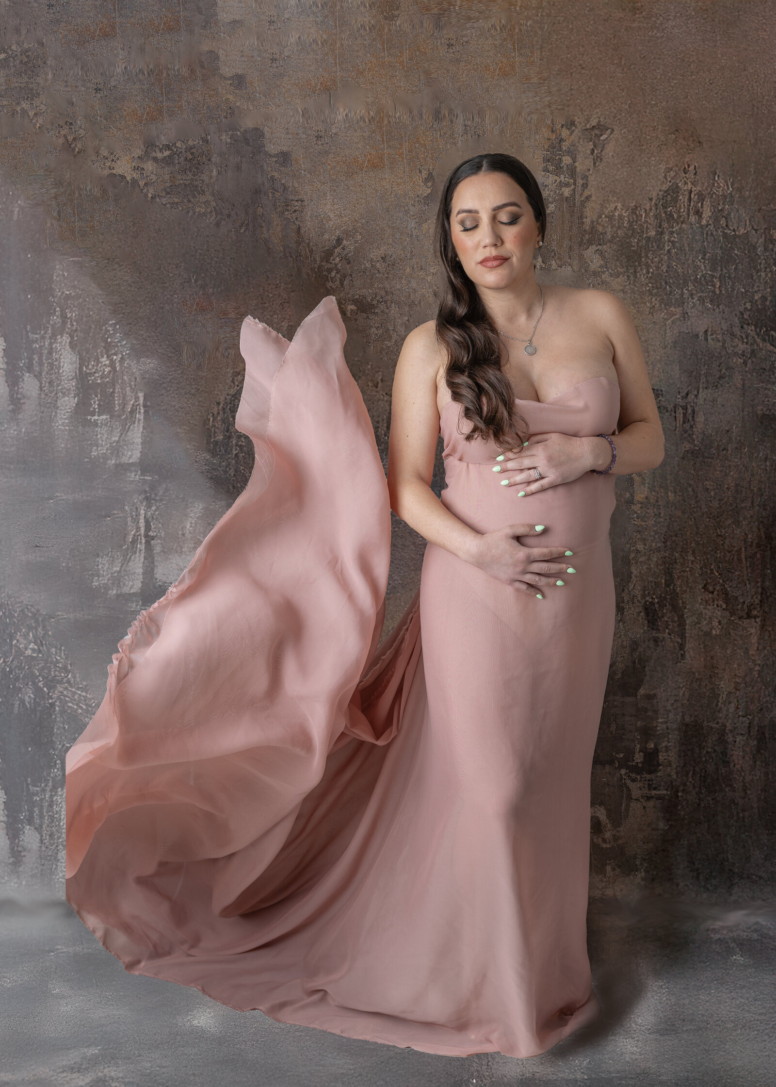 Pregnant woman in a flowing pink dress with the material flying up next to her during a maternity shoot in Bergen County, NJ.​