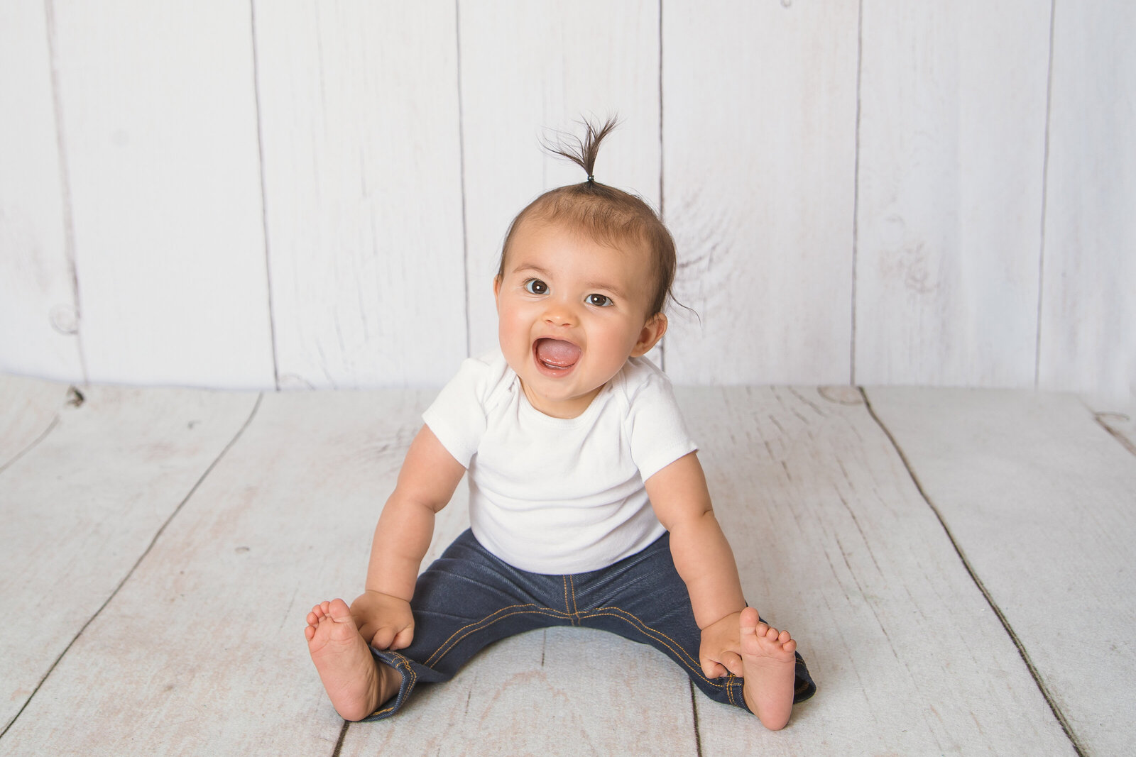 Milestone Photographer, a baby sits and smiles on wooden floors