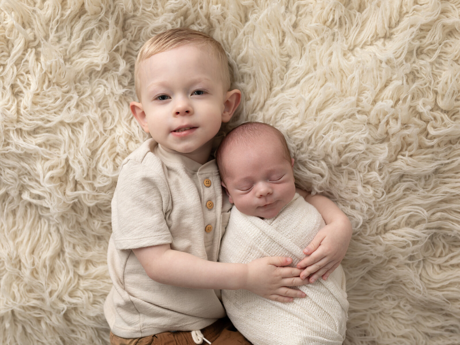 big brother holding newborn baby boy wrapped in white for studio portrait