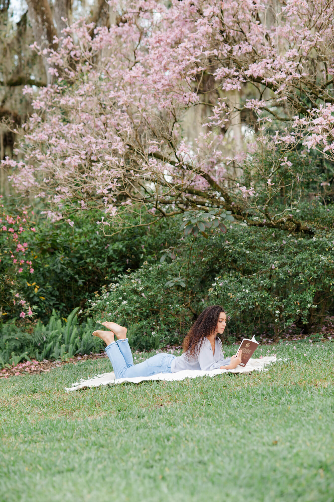 Senior laying in the grass at Bok Tower in front of the beautiful florals and reads a book during her senior session
