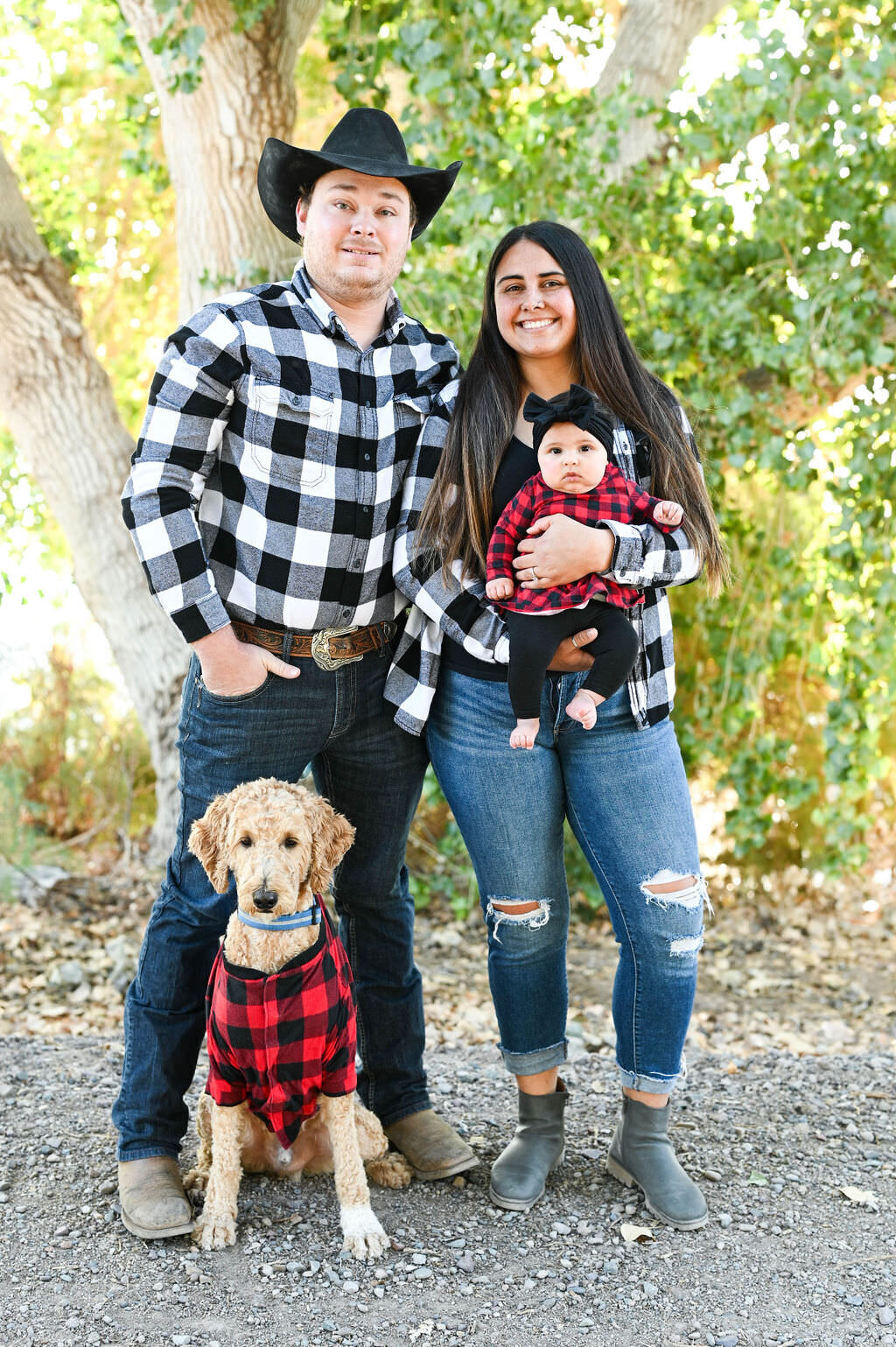 Parents holding a small child in their arms and posing in matching outfits with a dog sitting at their feet.
