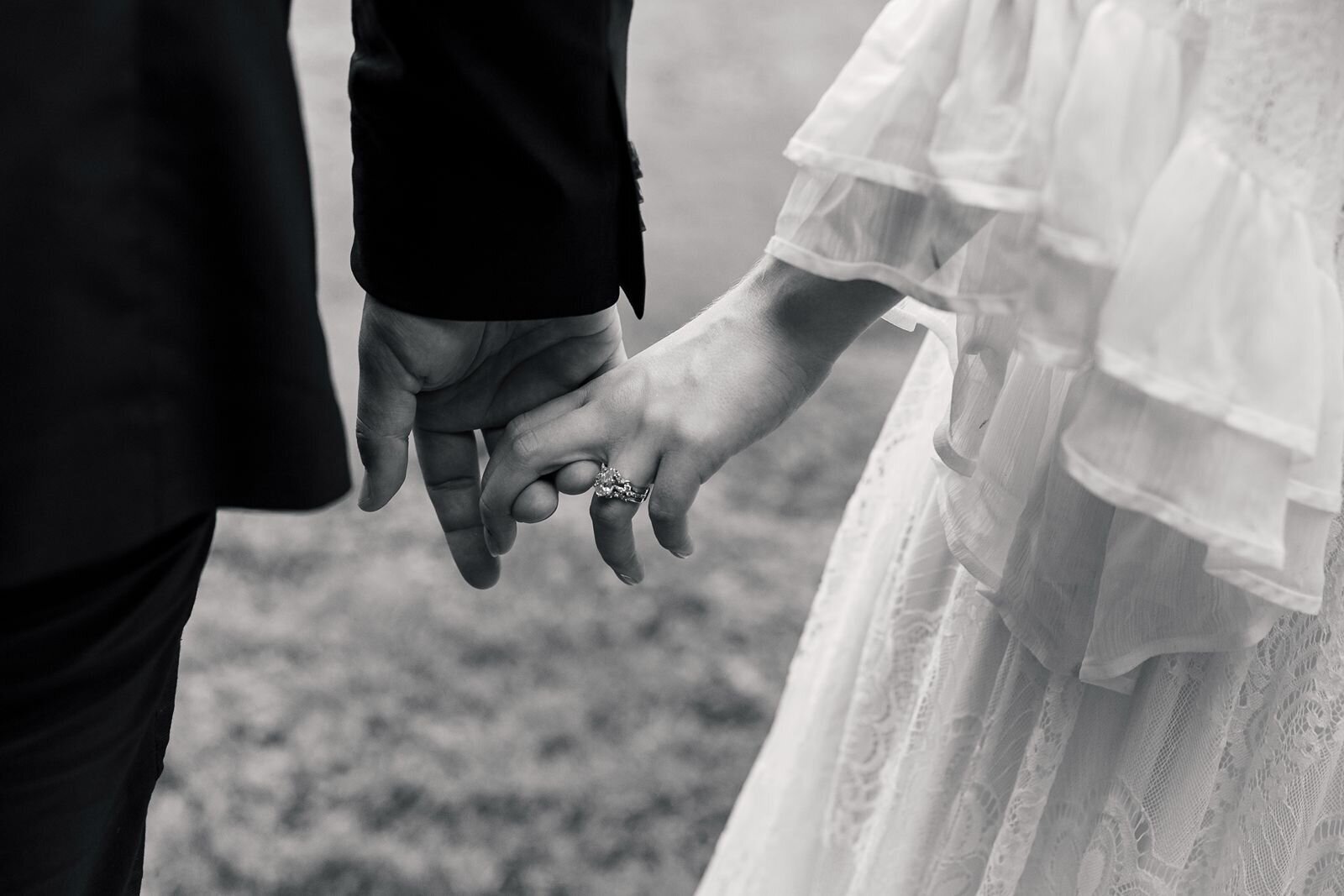 Black and white couple of a couple candid hand holding as they walk in the grass.