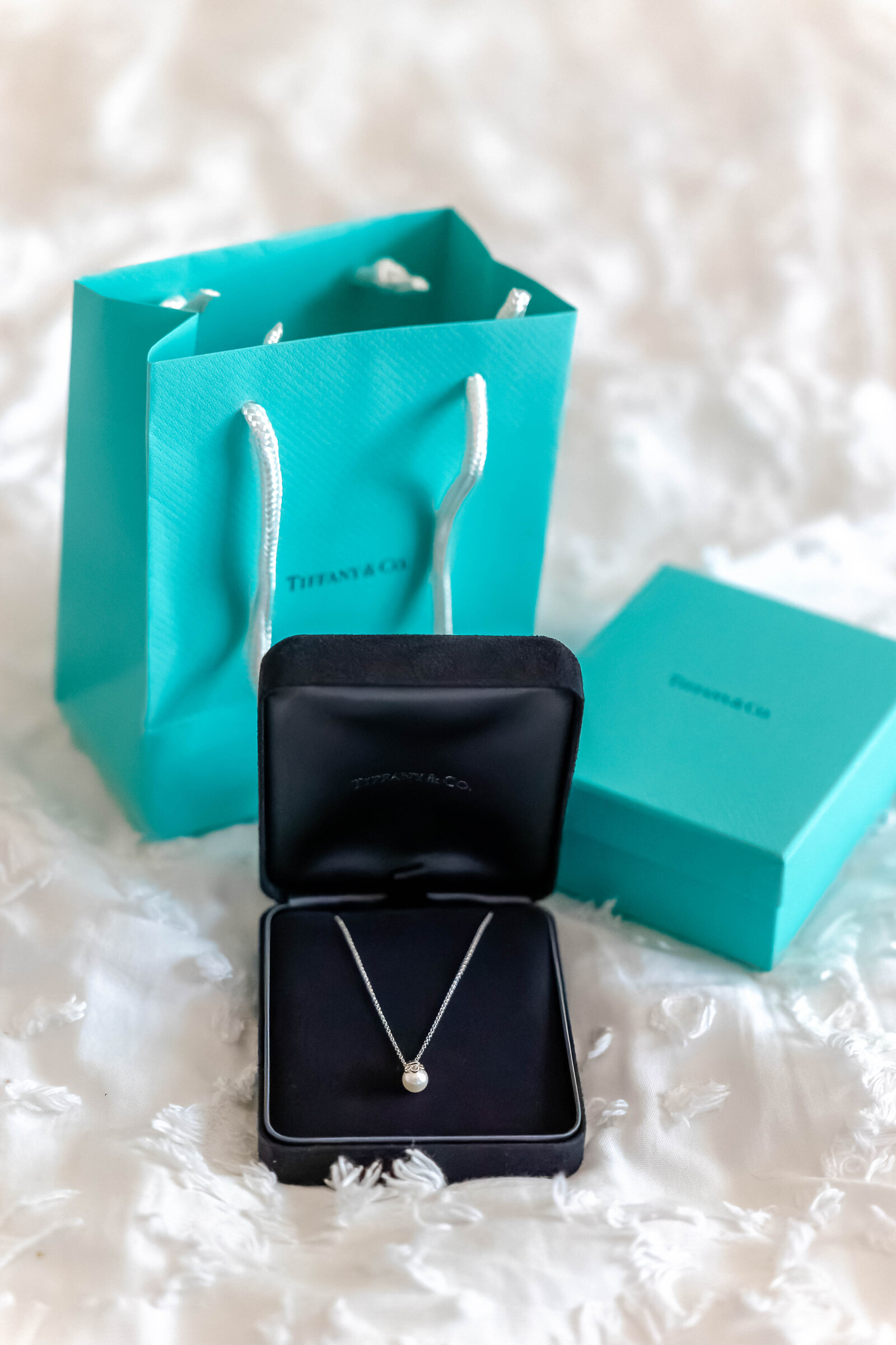 A Tiffany & Co. necklace displayed in an open box with the iconic blue bag and packaging in the background, captured during a Rodanthe, NC wedding in the beautiful Outer Banks, showcasing thoughtful and elegant bridal details.