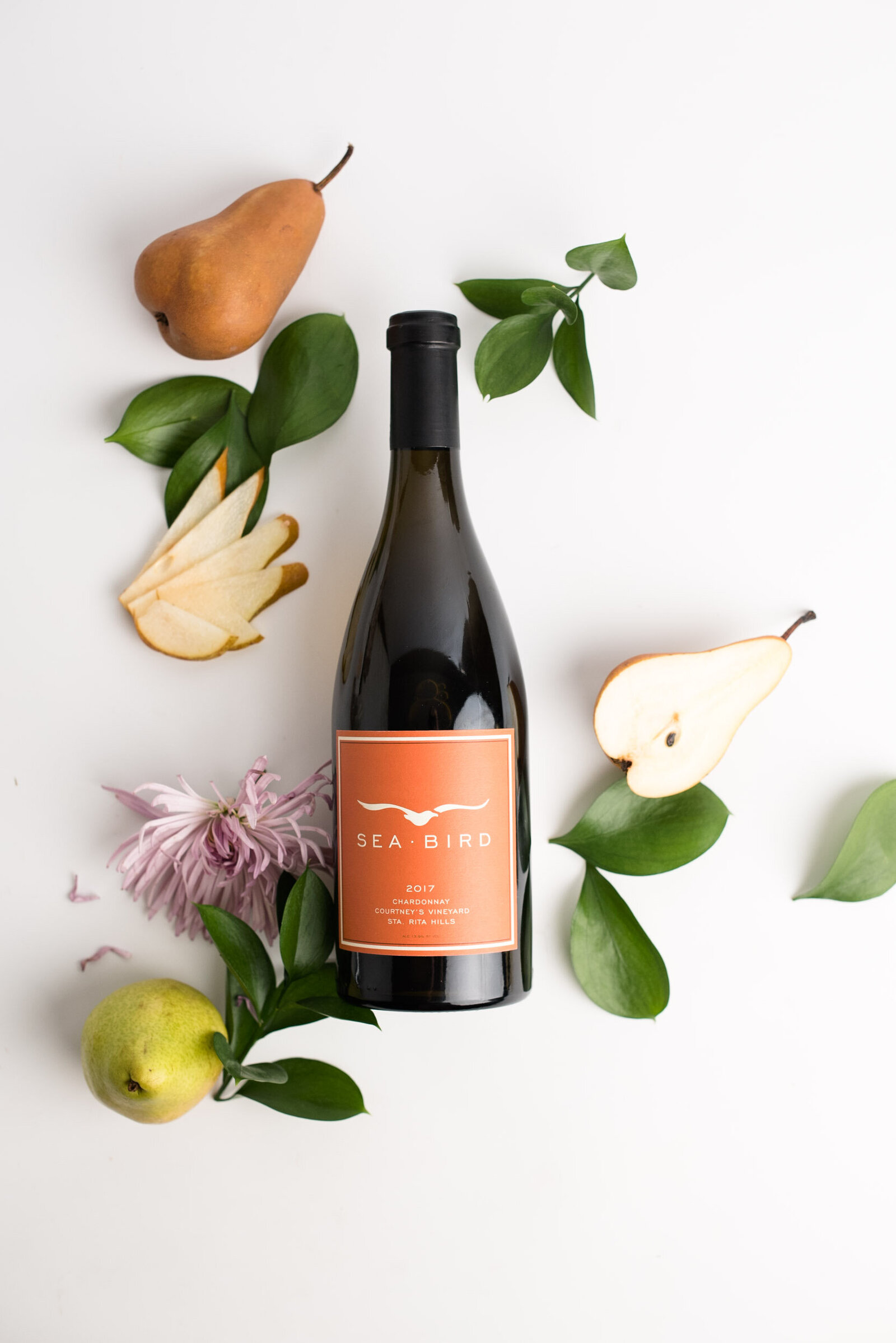 Bottle of wine laying on a white table with flowers and pears next to it