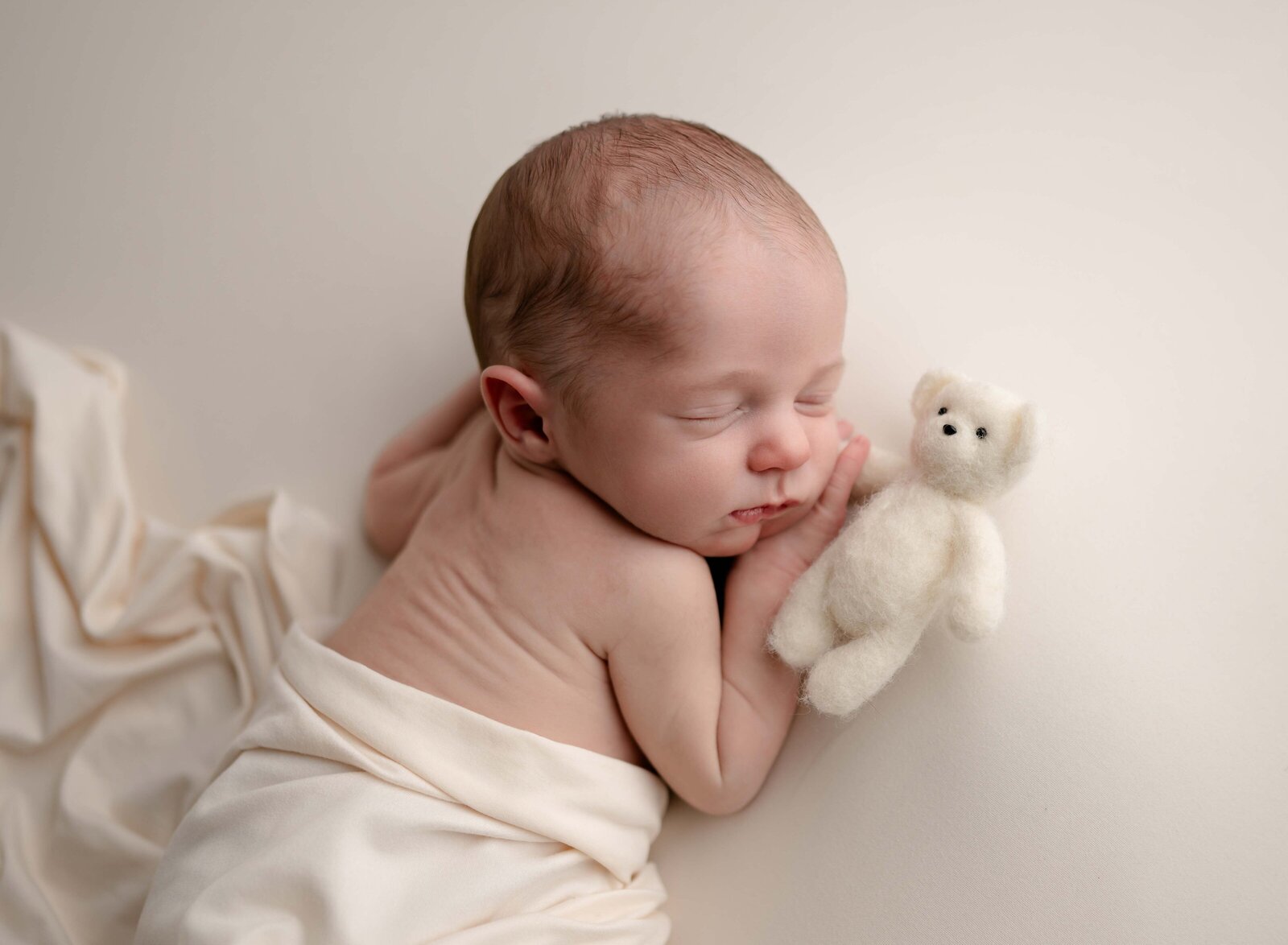 Baby sleeping on cream backdrop, holding teddy bear. Photo by Jenni Nikki Photography, Marietta Newborn photographer.