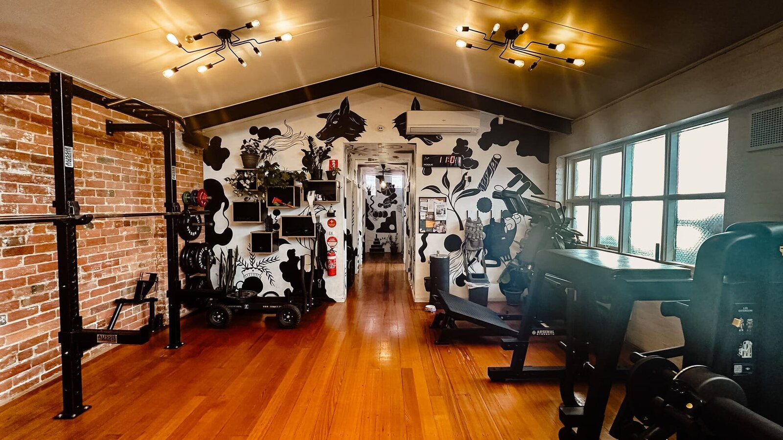 Weight racks at beautiful gym in Collingwood with wooden flooring and murals on the wall.