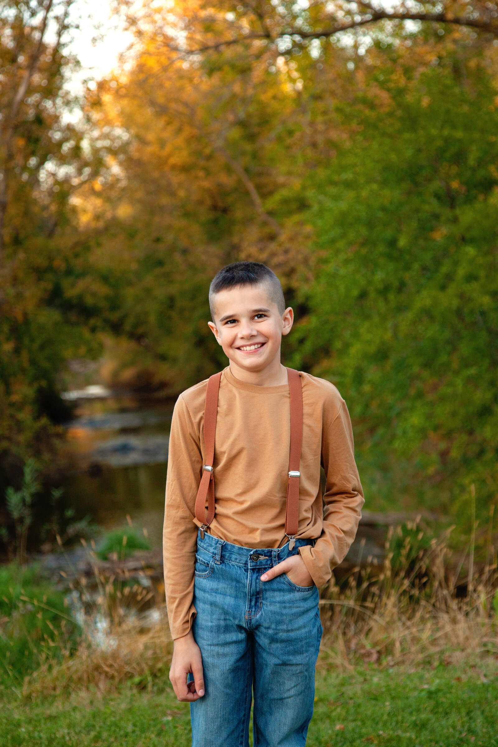 Boy with suspenders smiling, fall background.