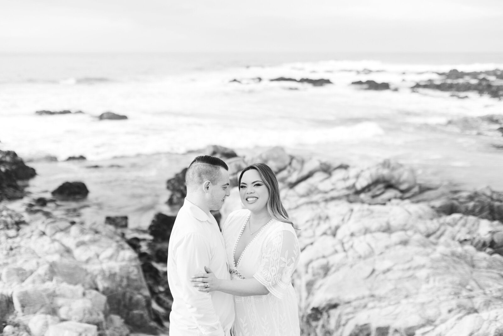 An engaged man and woman take photos on the beach in Pacific Grove, Monterey, California near Big Sur.