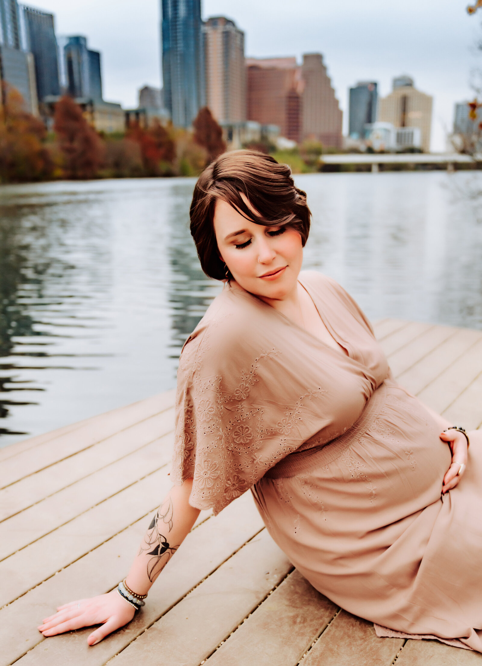 Maternity Photographer, a pregnant woman sits near the river in the city