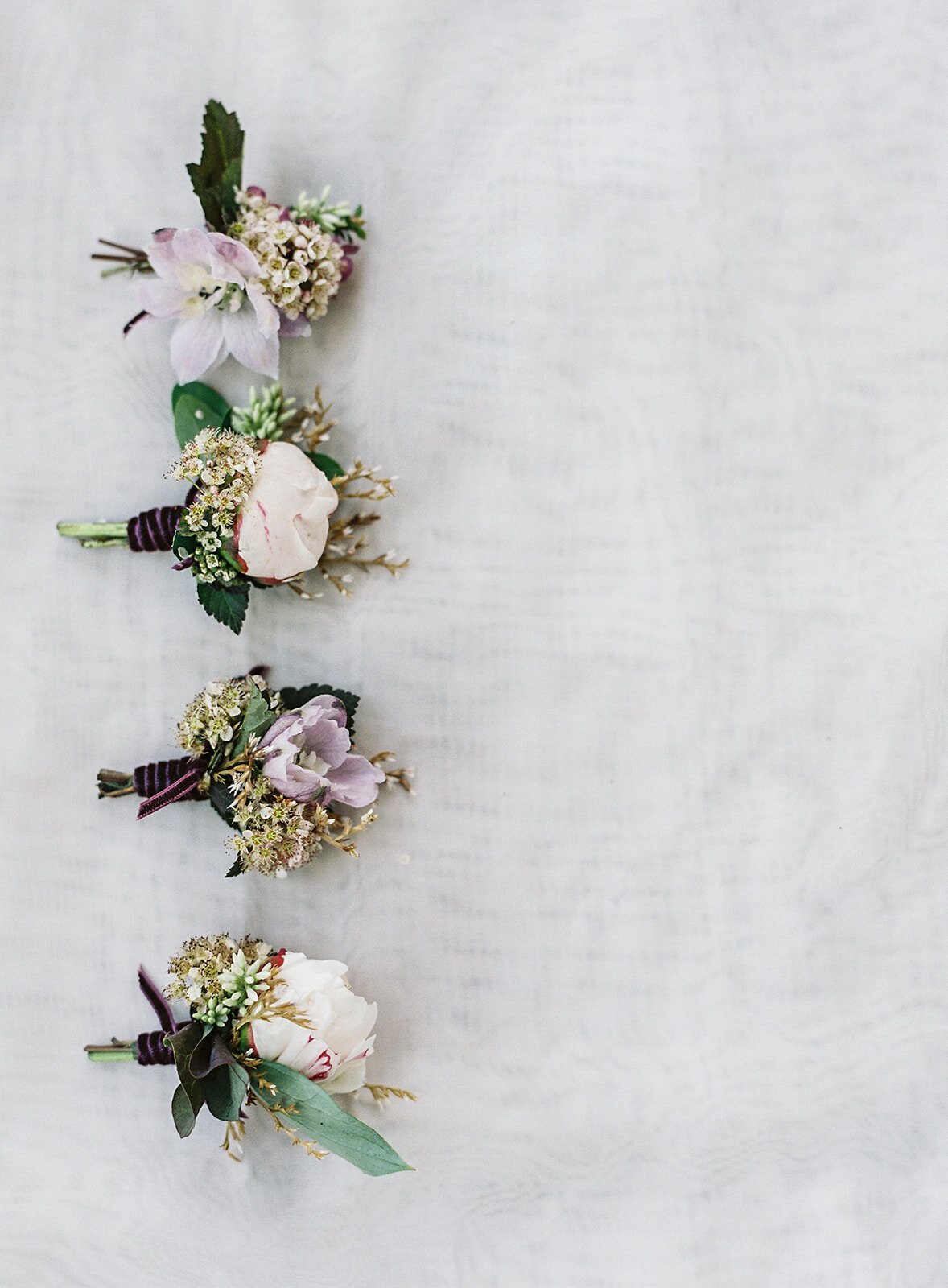 Four boutonnieres on the left side of frame spaced about an inch apart going from top to bottom. All in shade of purples and pinks. Photographed by wedding photographers in Charleston Amy Mulder Photography.